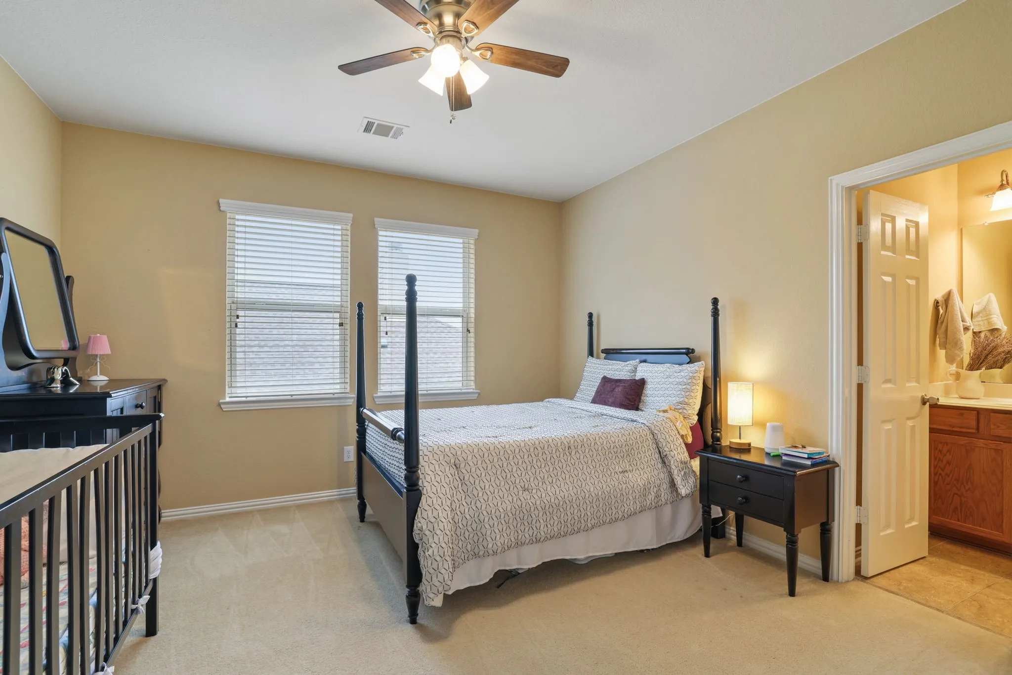 Carpeted room featuring two windows with blinds, a ceiling fan, and direct access to a bathroom
