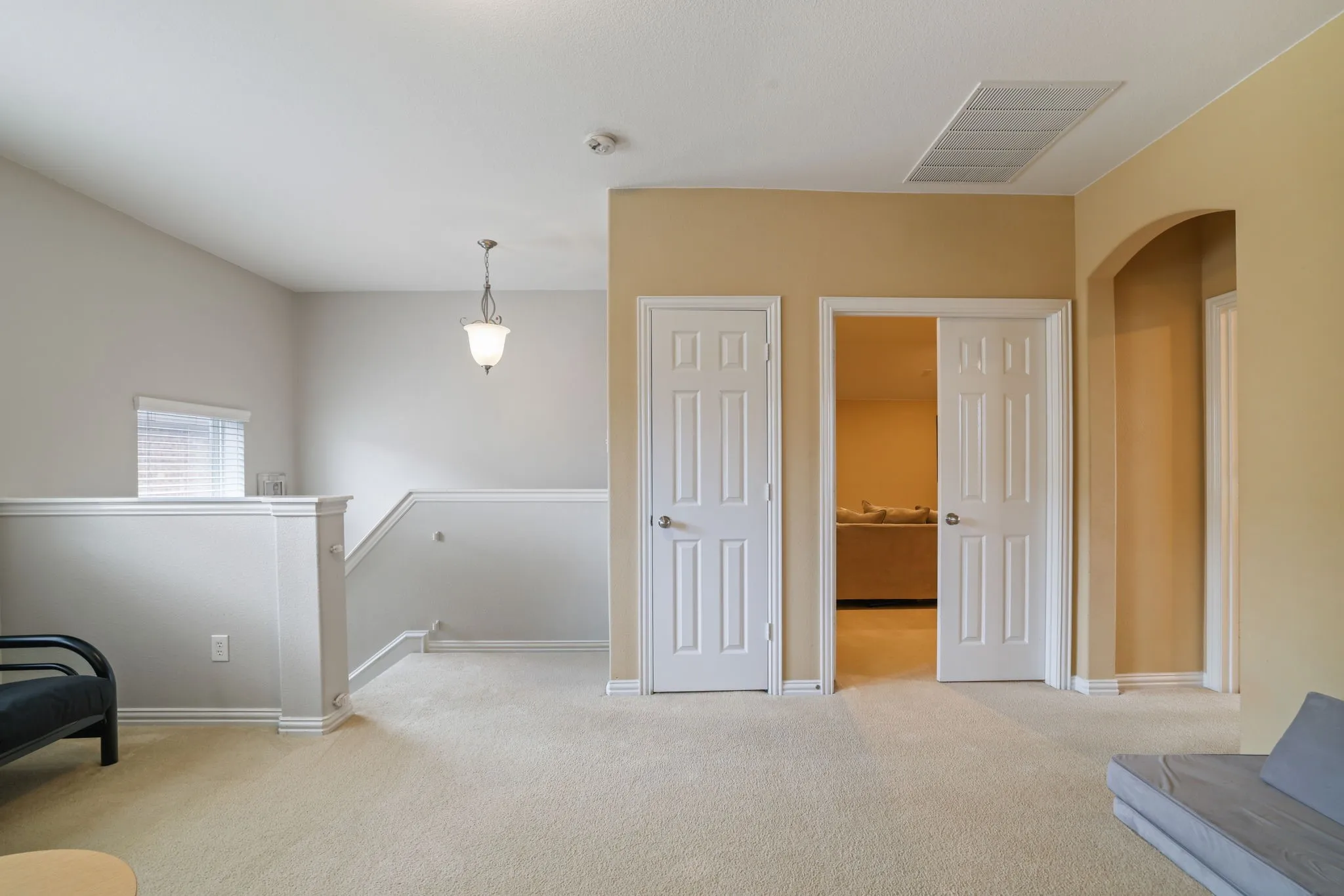 Carpeted landing area featuring two paneled doors, an arched doorway, and a traditional pendant light fixture