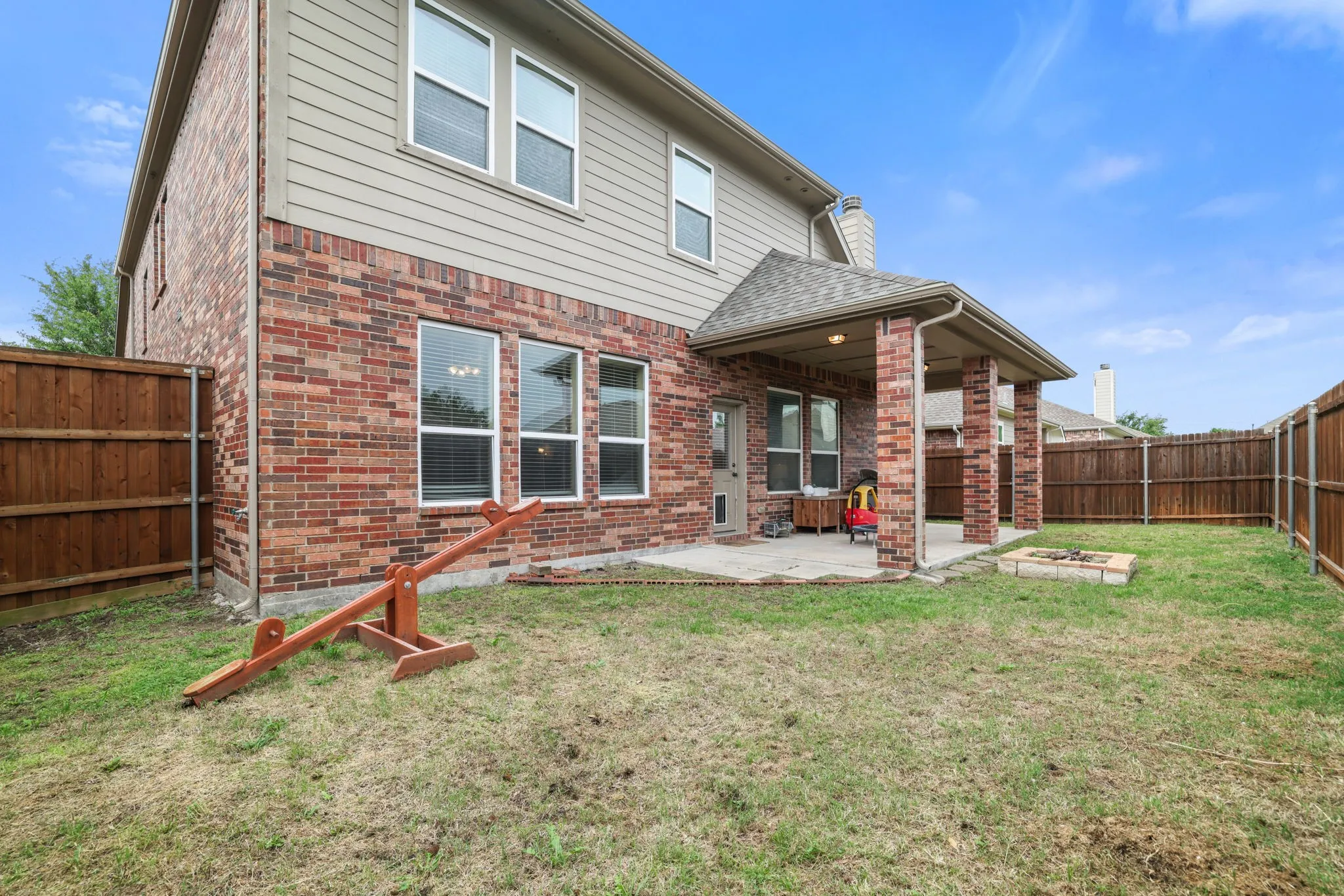 Expansive backyard featuring a covered patio, brick and siding exterior, fenced perimeter, and a built-in fire pit