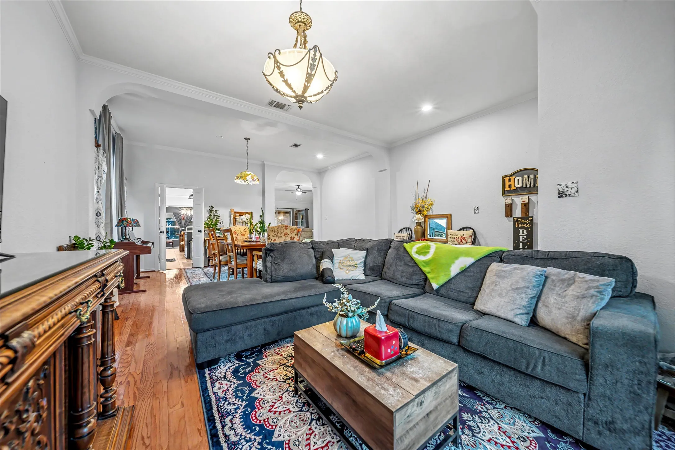 Spacious living area featuring wood-finish flooring, an ornate ceiling light fixture, recessed lighting, and crown molding