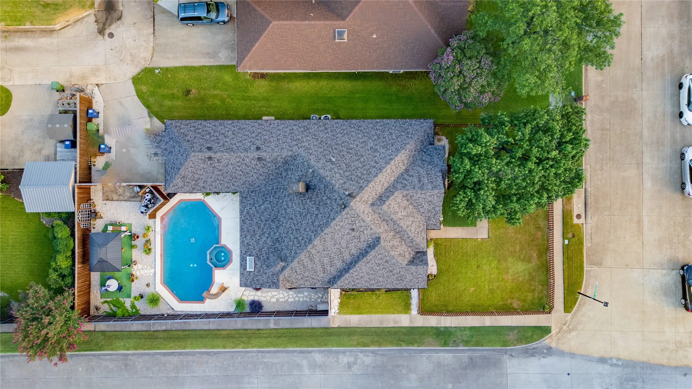 Expansive backyard featuring a geometric-shaped pool with integrated spa, a stone patio, and perimeter fencing