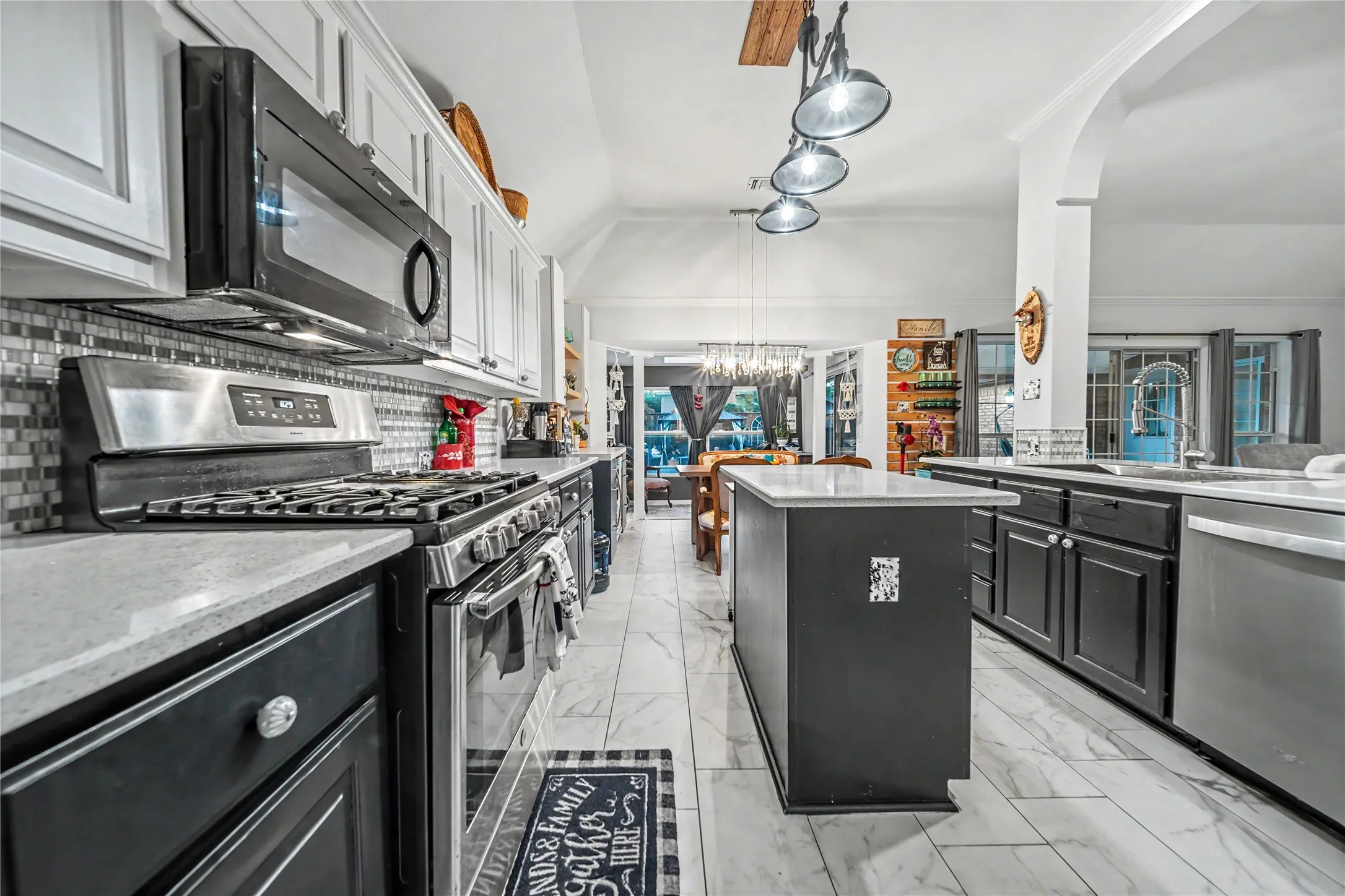 Spacious kitchen featuring an island, stainless steel appliances, white cabinetry, dark lower cabinetry, and a tile backsplash