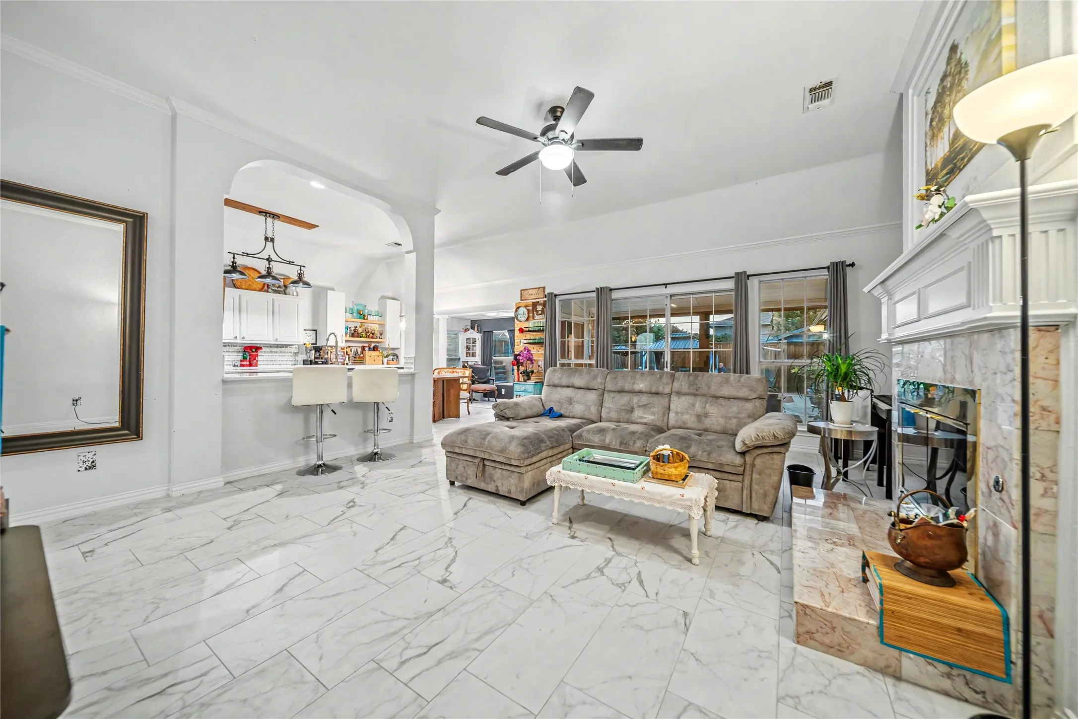 Spacious interior featuring a white mantel fireplace with tile surround, marble-look tile flooring, and an arched entry to the kitchen