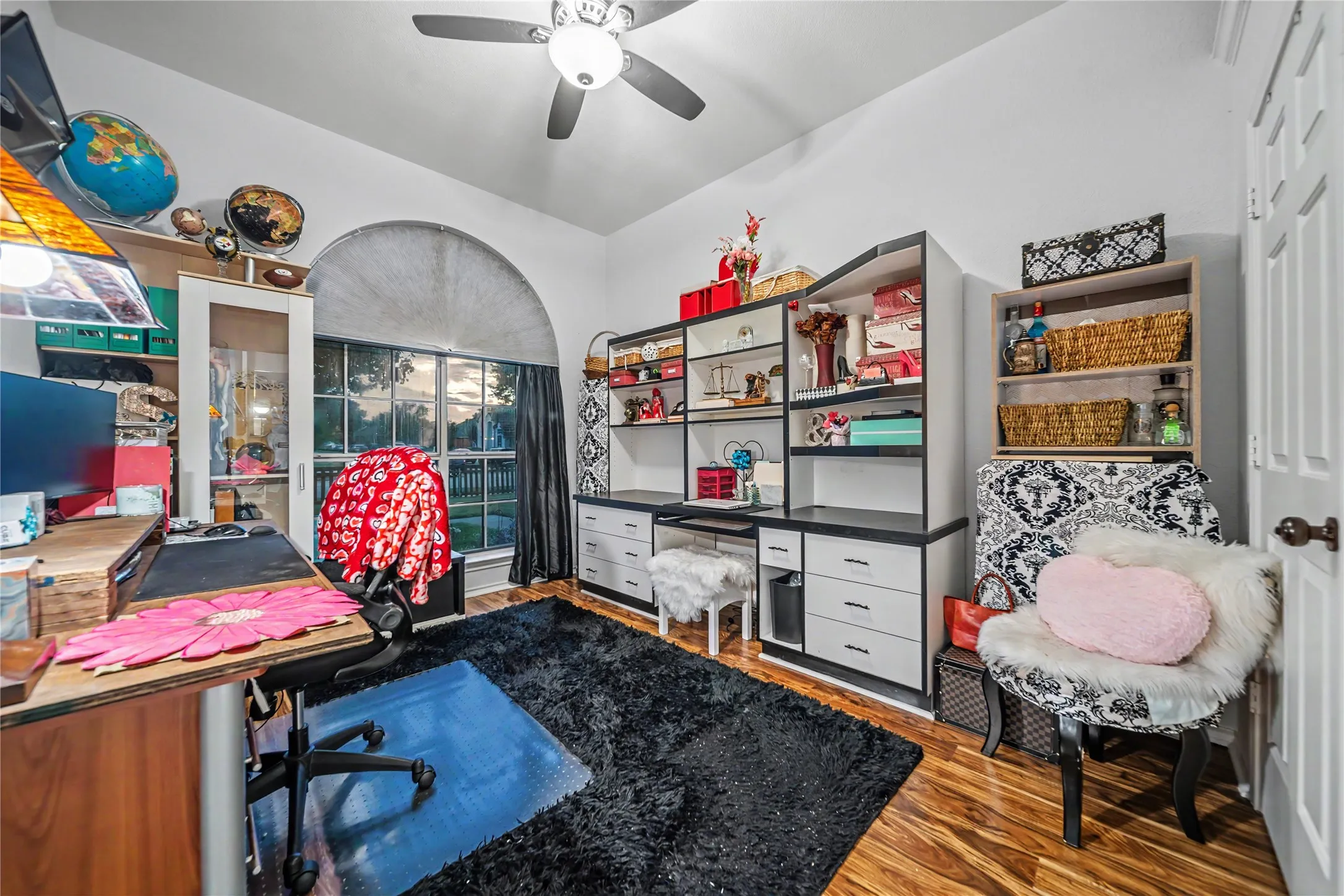 Room featuring wood-finish flooring, an arched window with blinds, and white walls