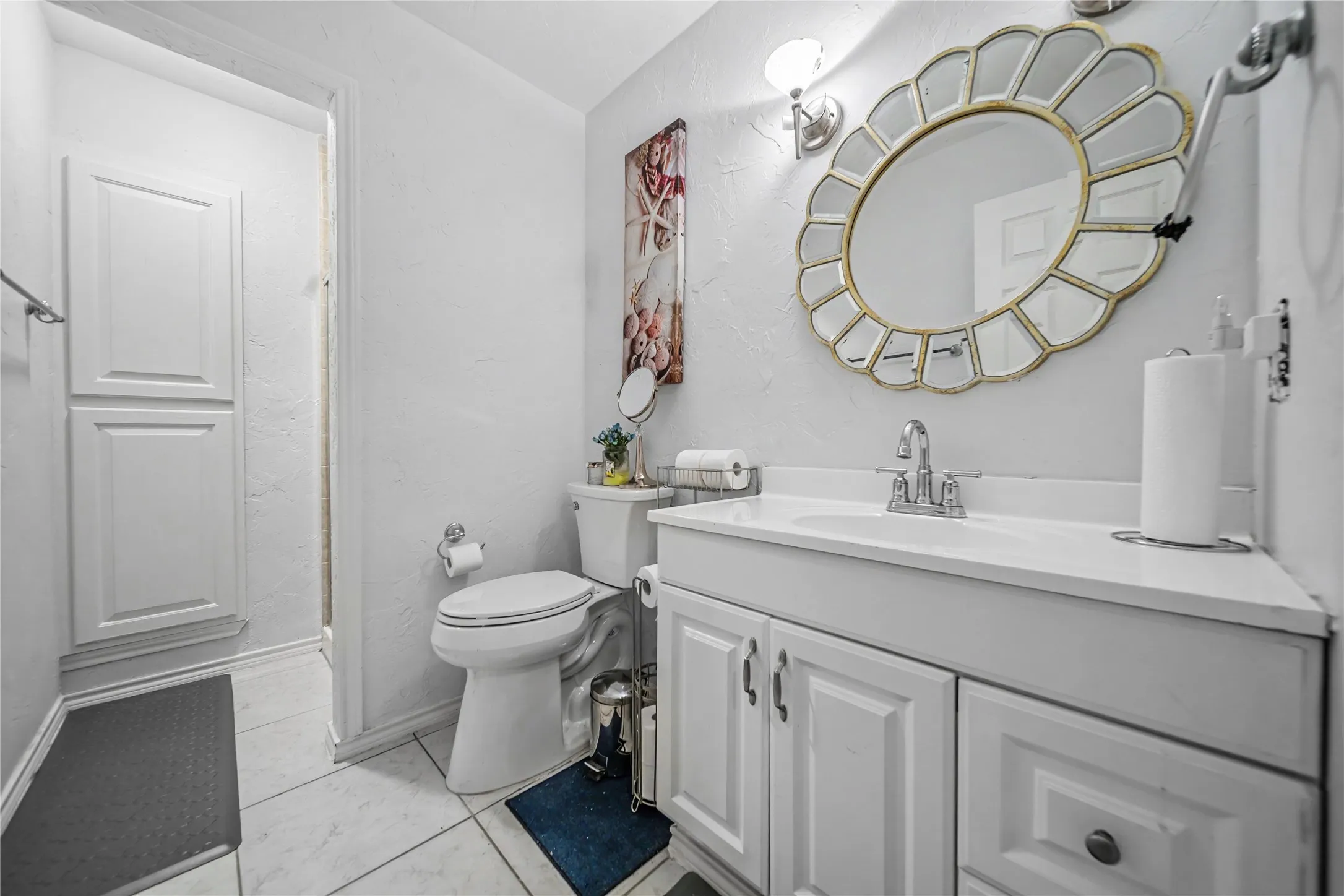 Bathroom adjacent to bonus room, featuring a single vanity with white cabinetry, a built-in sink, and a decorative round mirror
