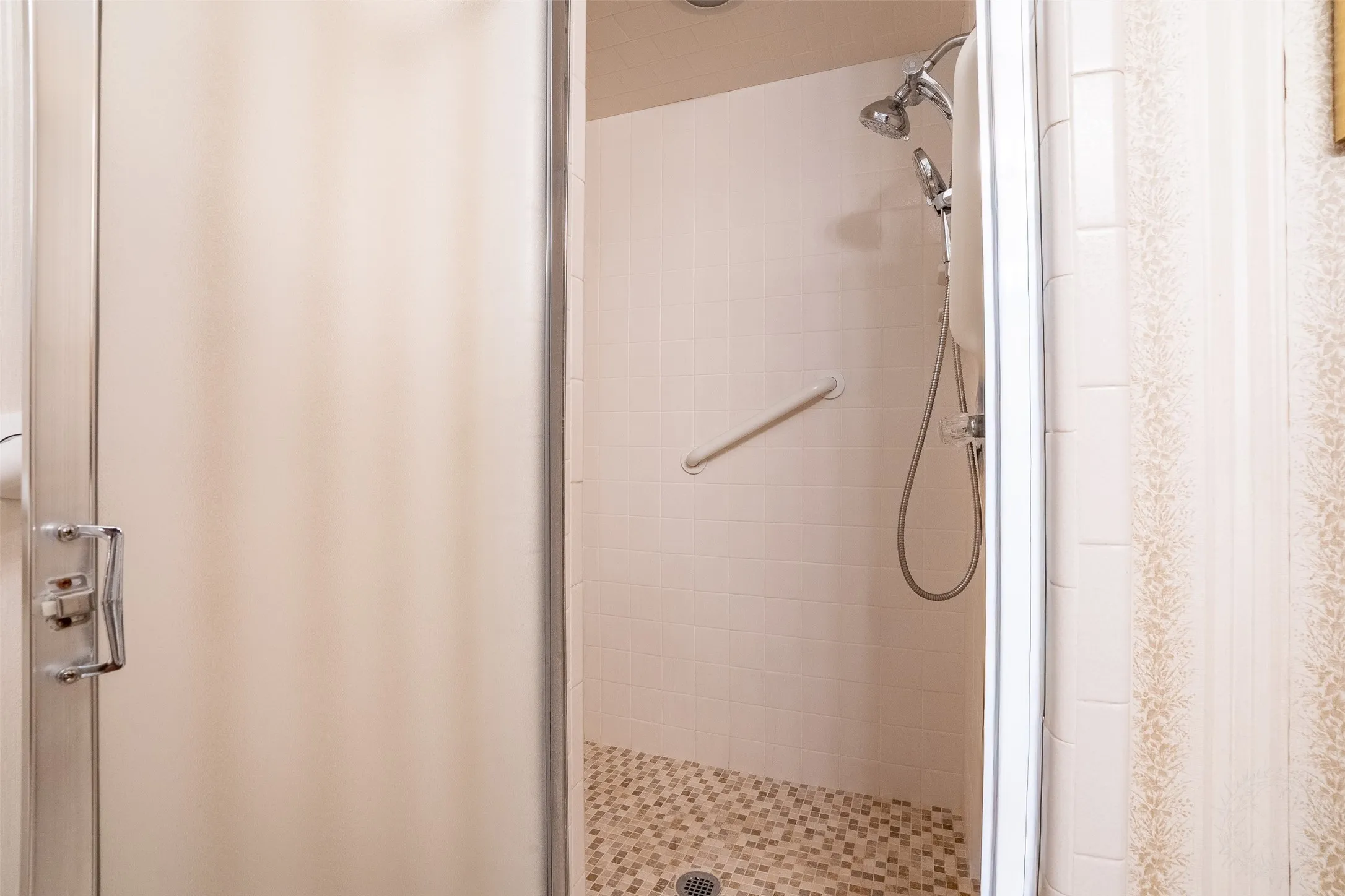 Shower enclosure with frosted glass door, mosaic tile flooring, a wall-mounted grab bar, and a dual shower head system