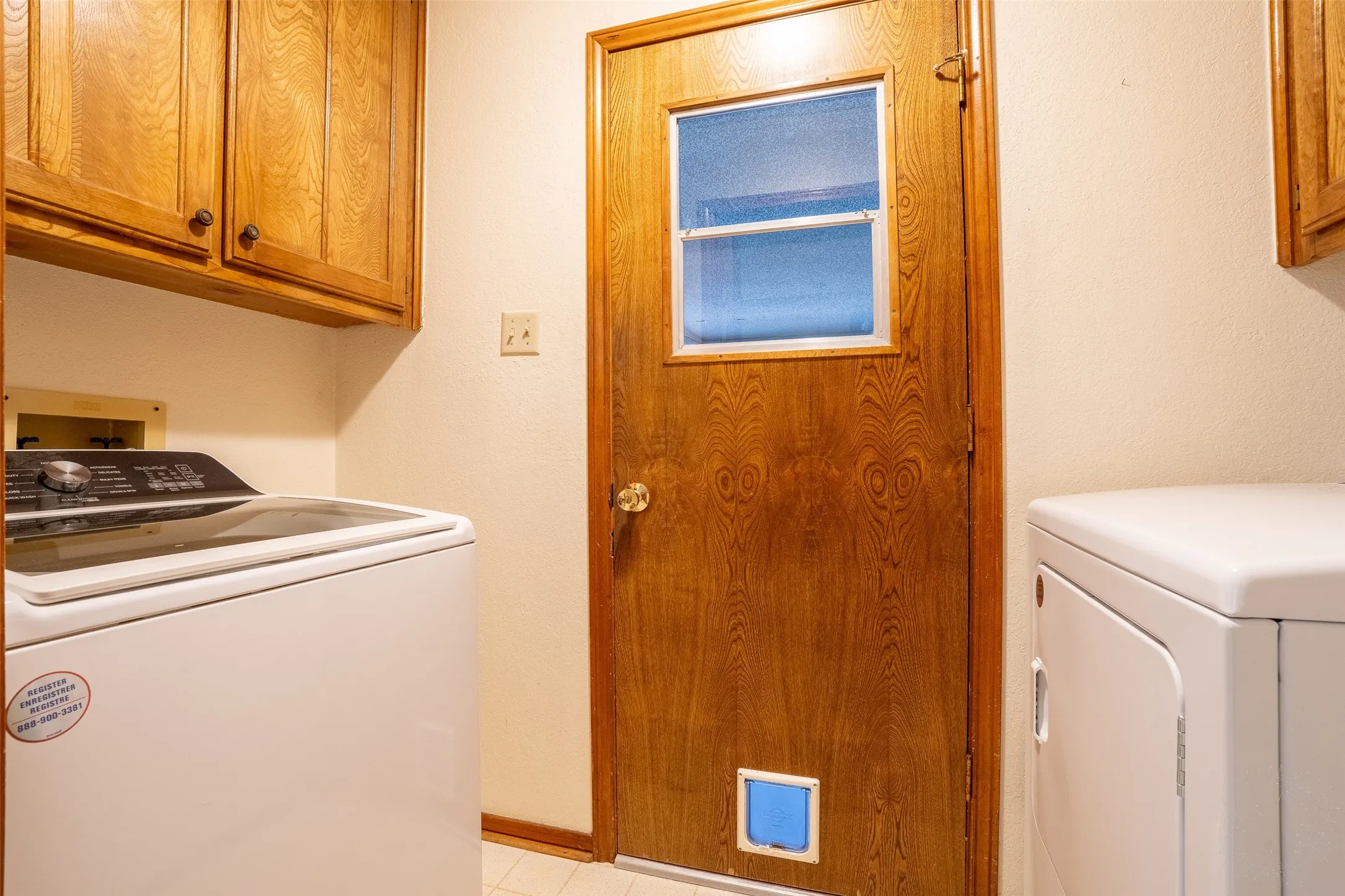 Utility room with light wood-finish cabinetry, a wood-finish door featuring a window, and durable flooring