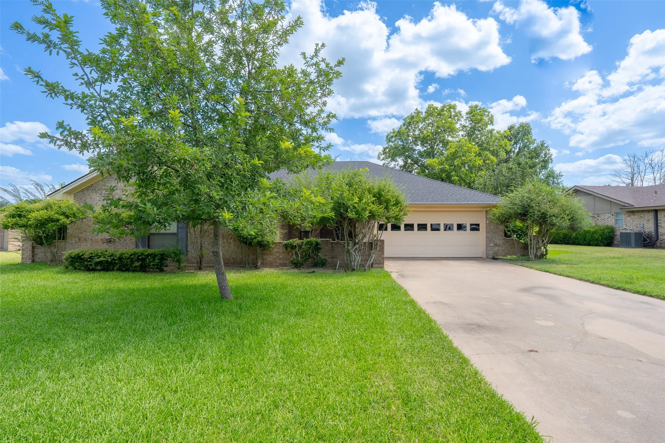 Brick exterior featuring a two-car garage with panel windows, a concrete driveway, and mature landscaping