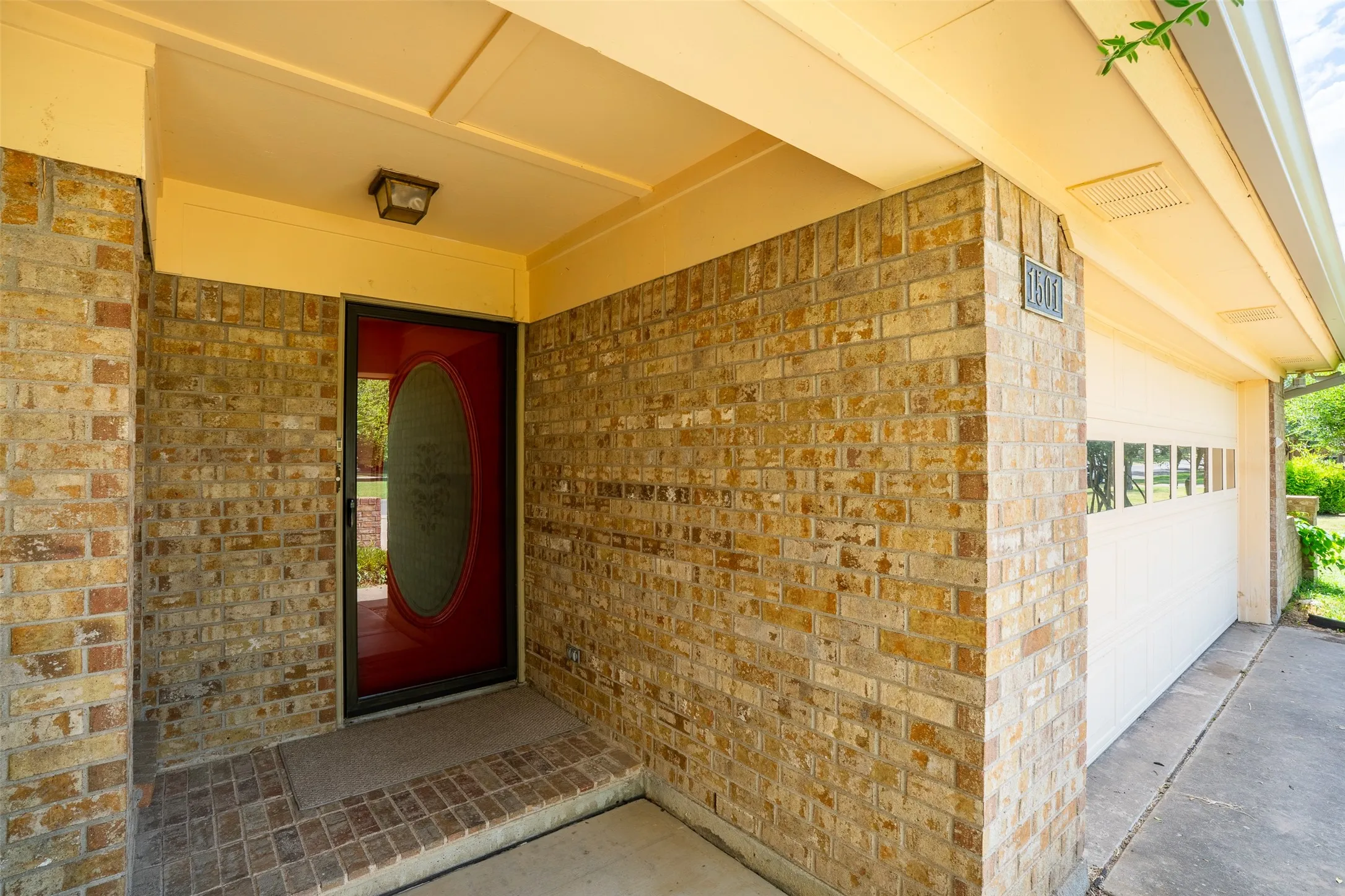 Brick facade entryway with an oval-lite red door and matching brick-laid porch