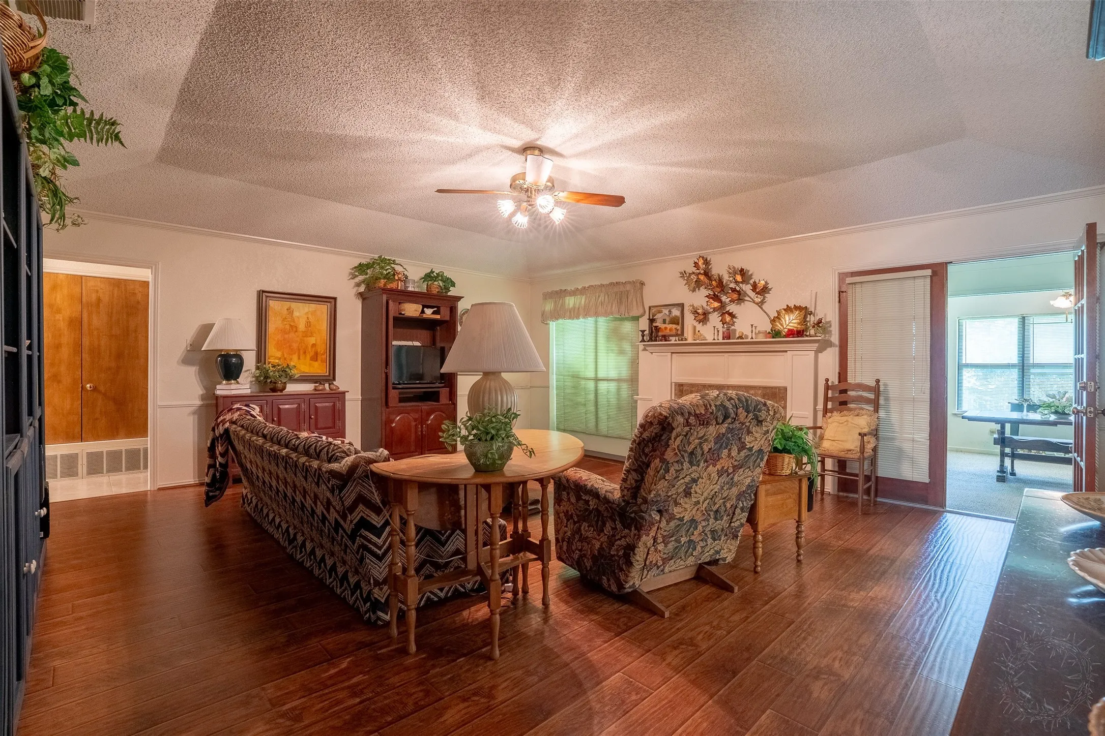 Living area featuring wood-finish flooring, a fireplace with a white mantel, and a ceiling fan