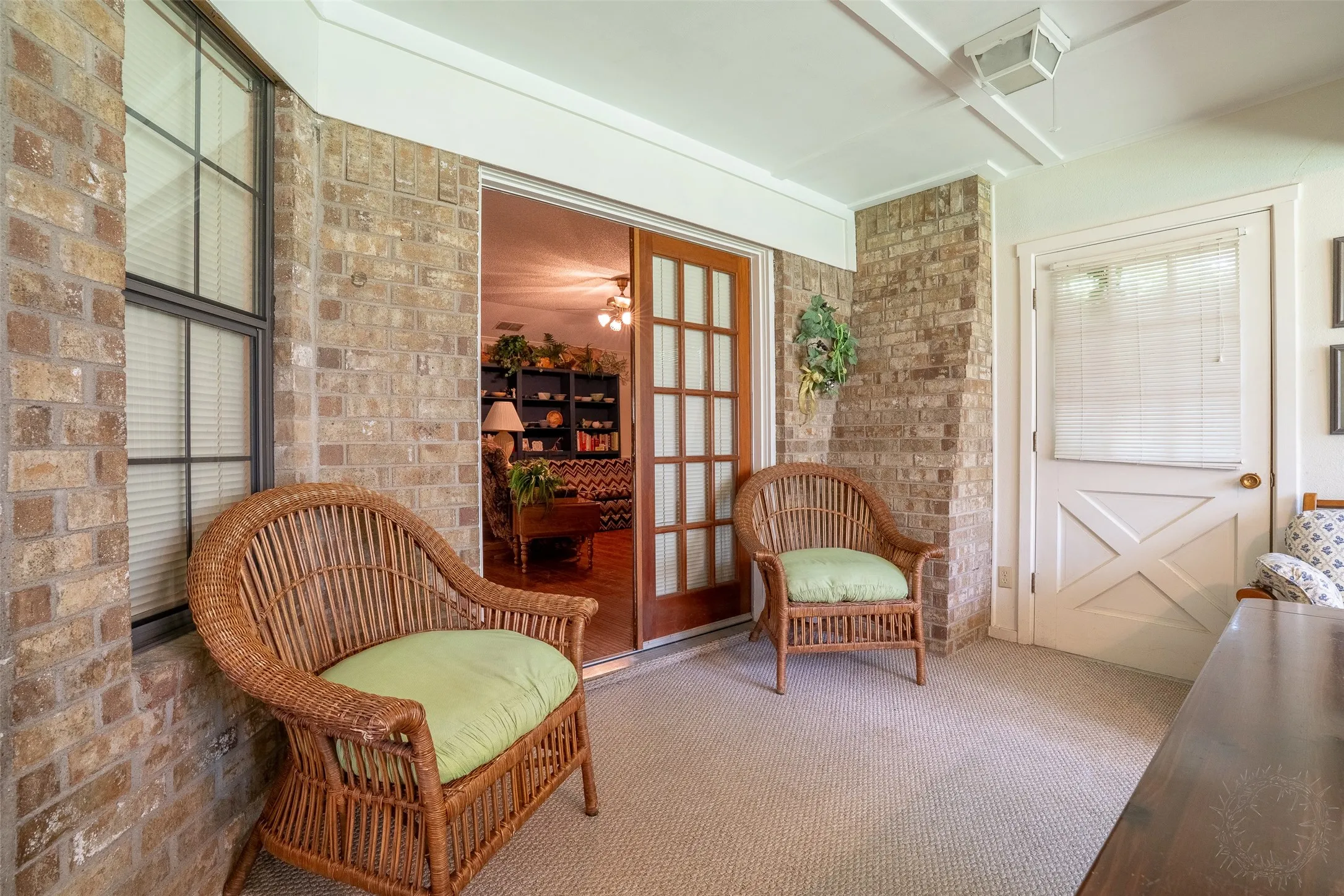 Enclosed porch featuring light brick walls, a white paneled ceiling, and light-colored carpet flooring