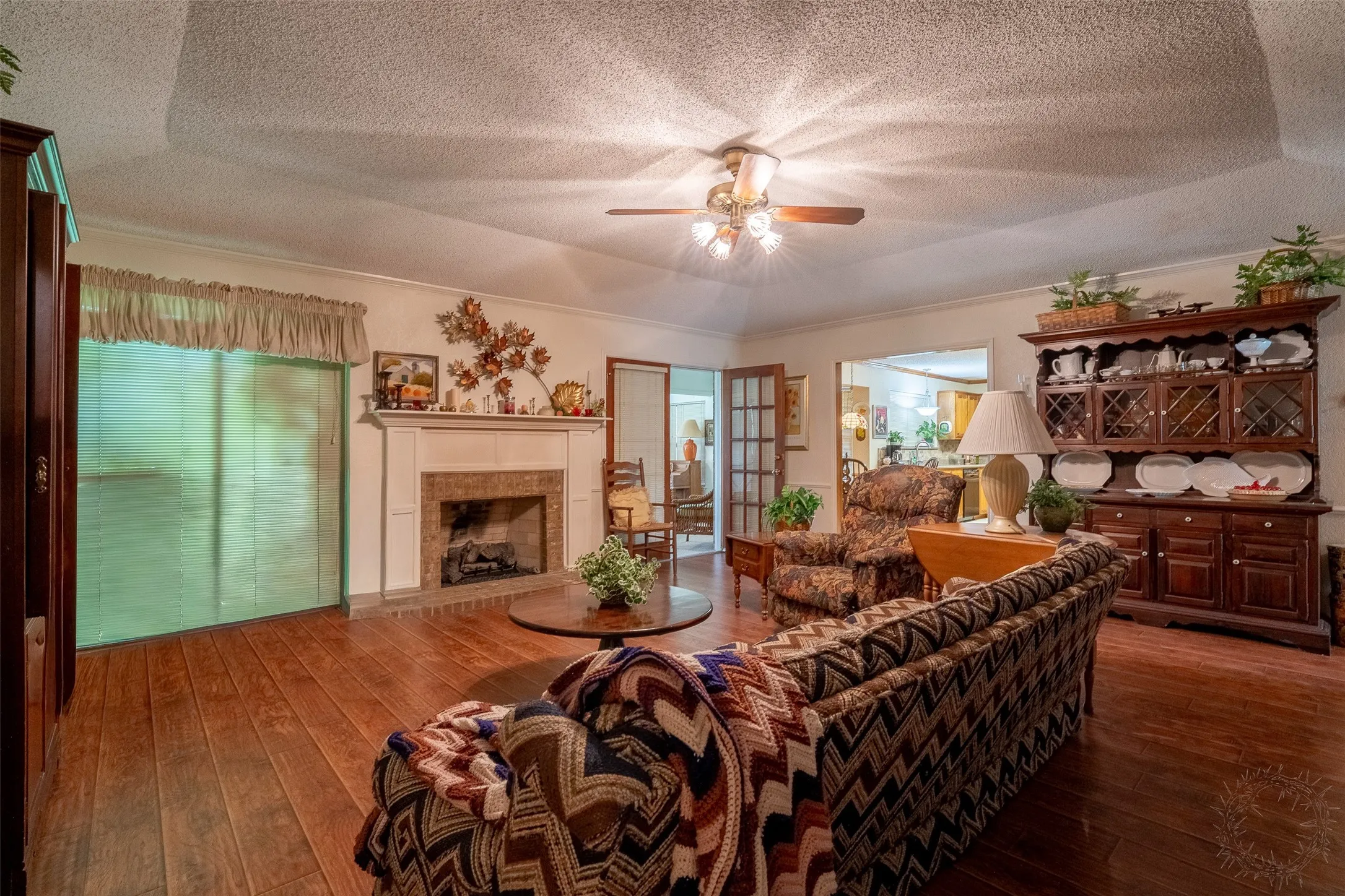 Living room featuring wood-finish flooring, a tray ceiling, and a fireplace with a white mantel and stone surround