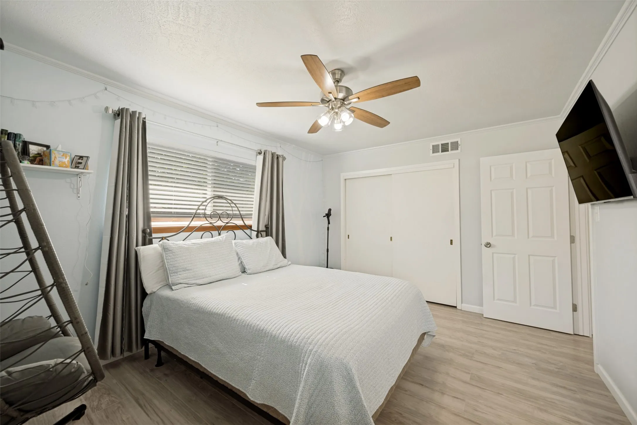 Bedroom featuring wood-finish flooring, a ceiling fan with light fixture, a window with blinds and drapes, and a built-in closet with sliding doors