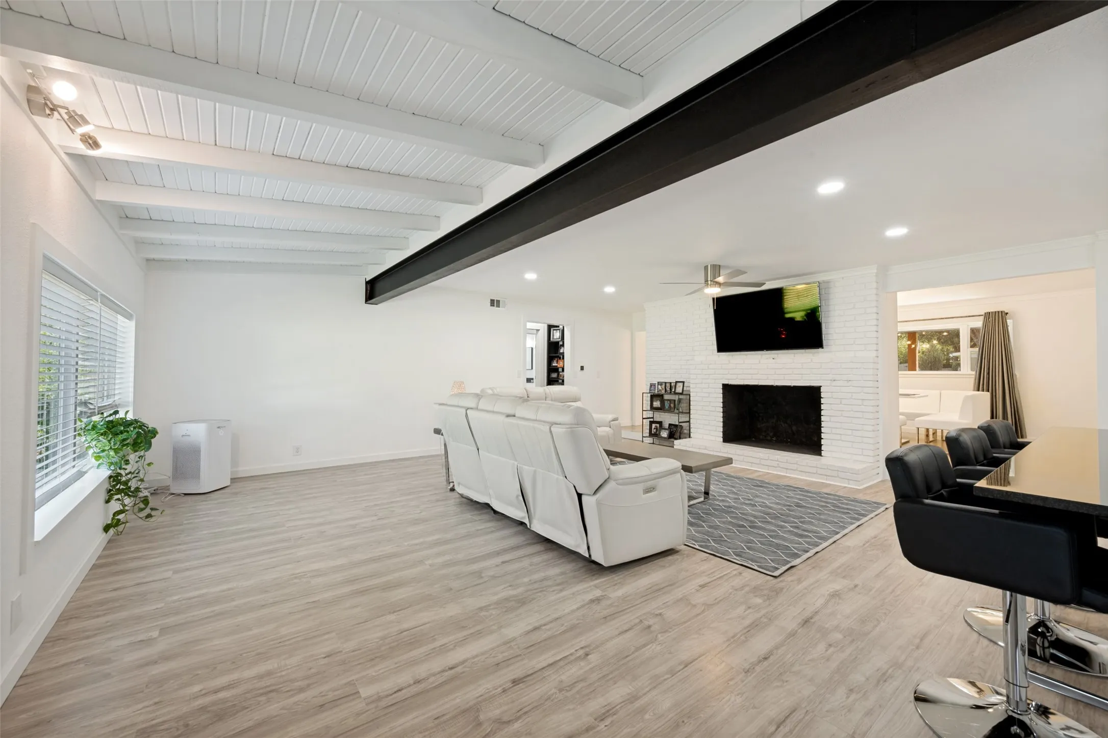 Spacious living area featuring light colored flooring, exposed wood beam ceiling, and a prominent dark structural beam