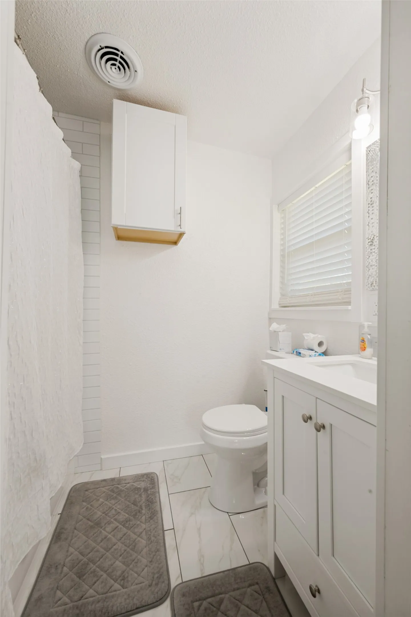 Bathroom featuring a single vanity with storage, a toilet, and a shower area with subway tile surround