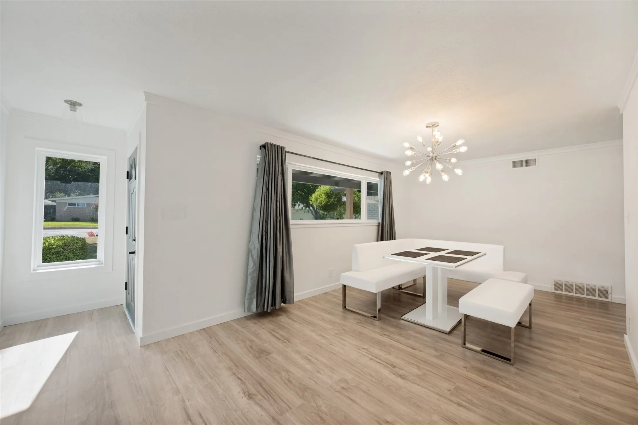 Bright interior space featuring wood-finish flooring, white walls, and a contemporary chandelier
