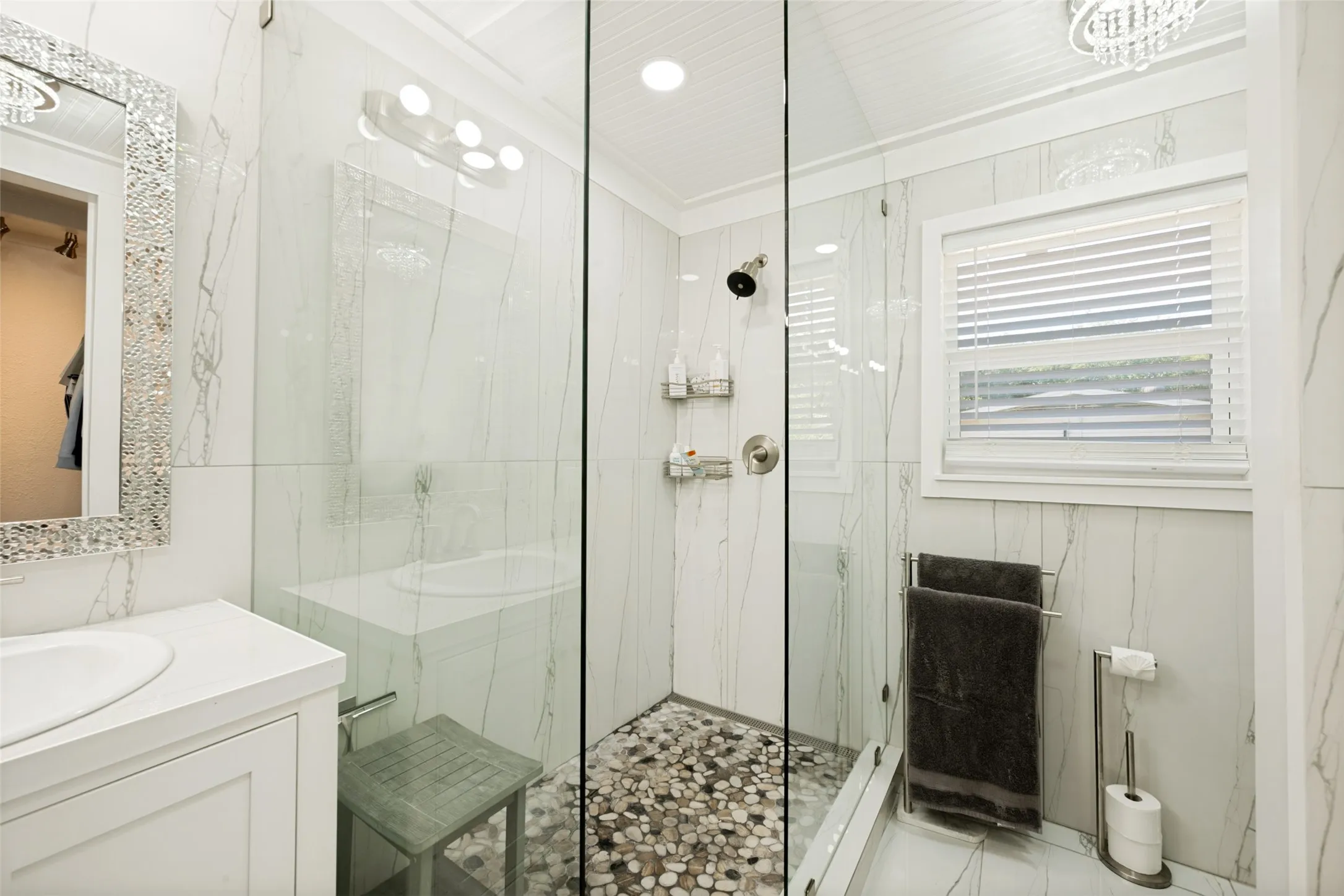 Modern bathroom featuring a glass-enclosed shower with pebble-style flooring, and a built-in window