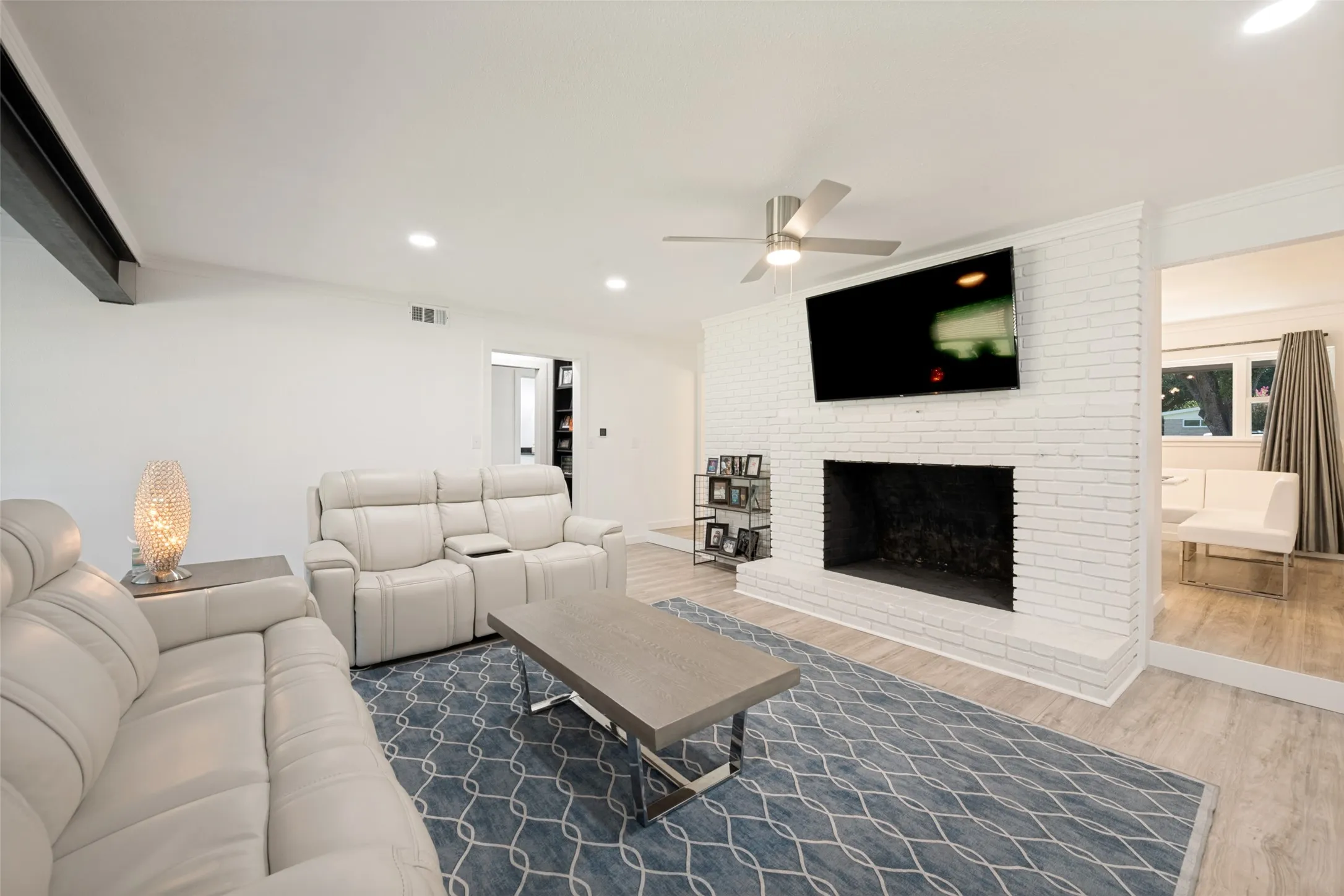 Living room featuring a whitewashed brick fireplace, a ceiling fan with integrated lighting, wood-look flooring, and recessed lighting