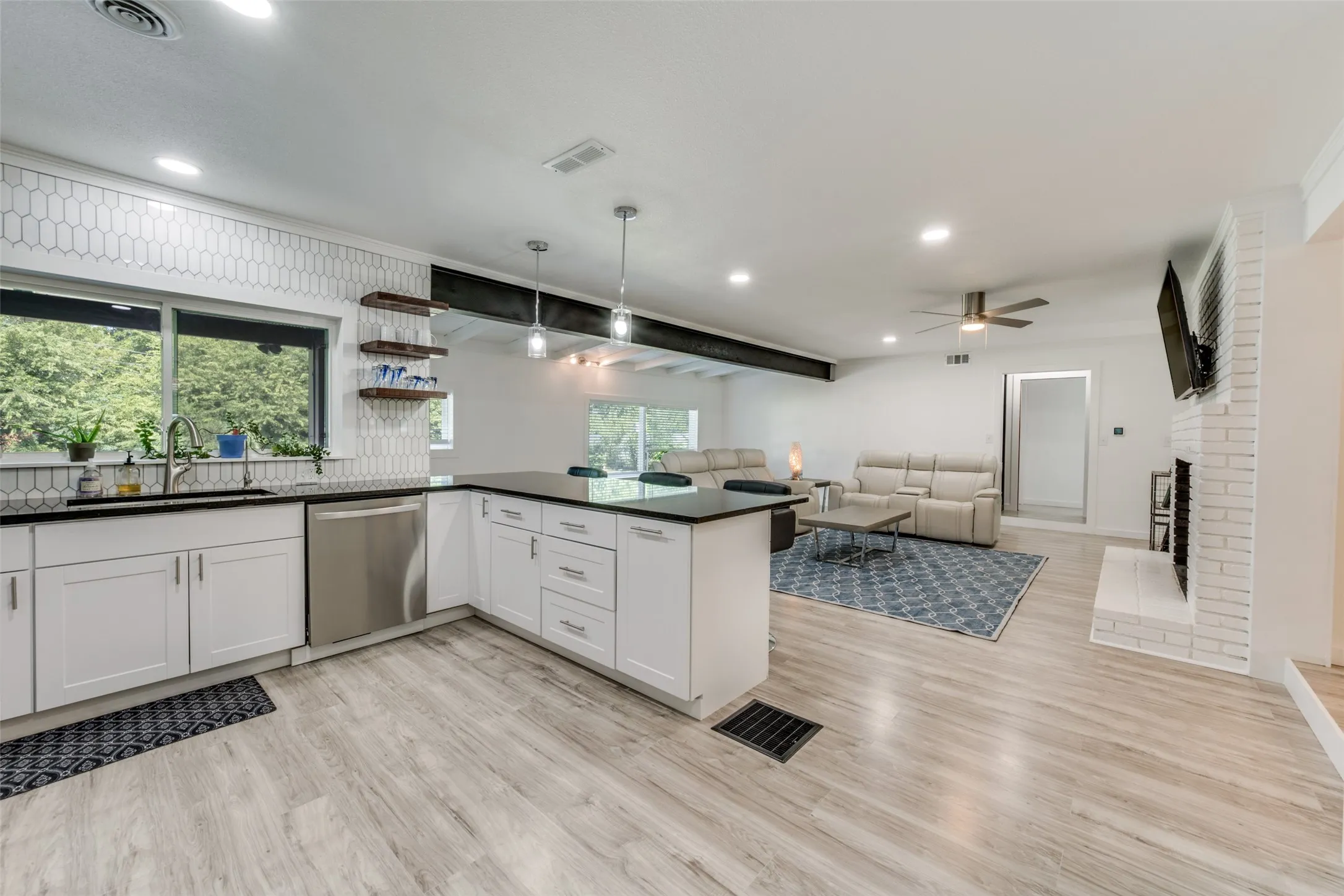 Open-concept living space featuring a modern kitchen with white cabinetry, dark countertops, and a picket tile backsplash