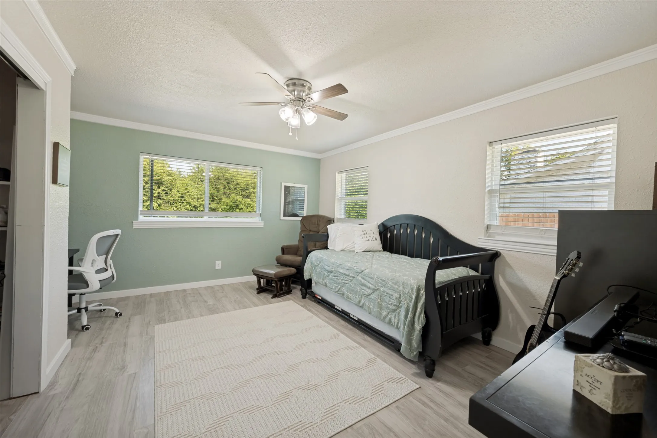Spacious room featuring light wood-look flooring, a ceiling fan, and multiple windows providing natural illumination