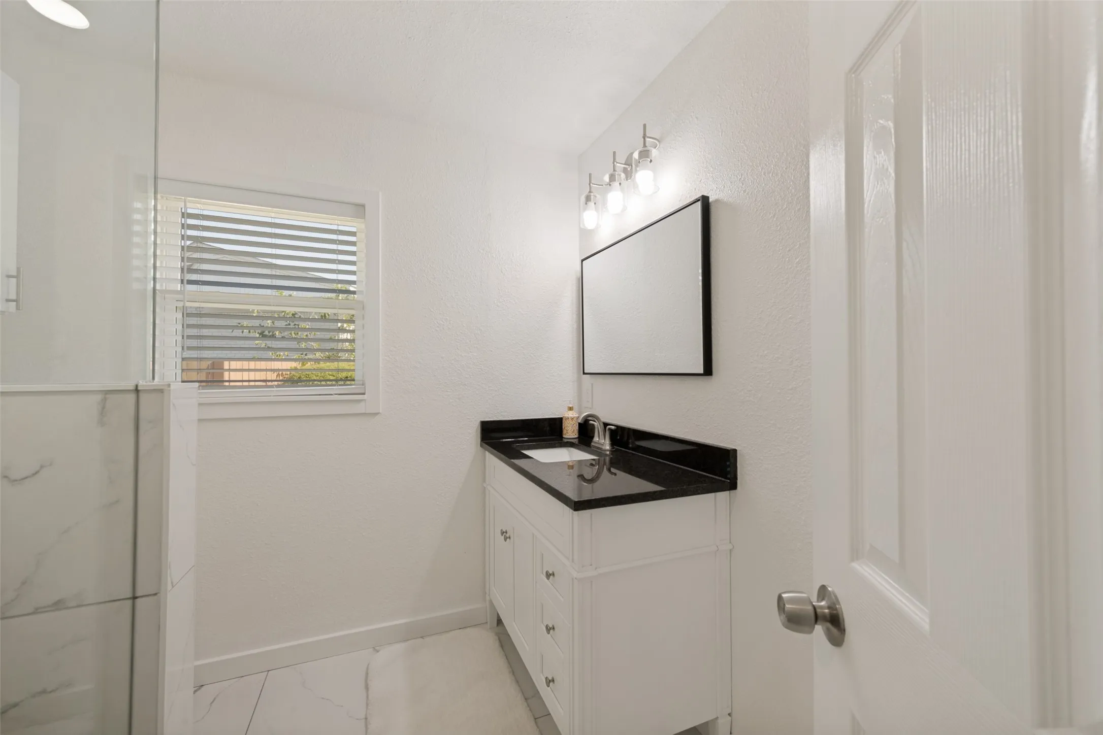 Bathroom featuring a white vanity with a dark countertop, an undermount sink, and a framed mirror