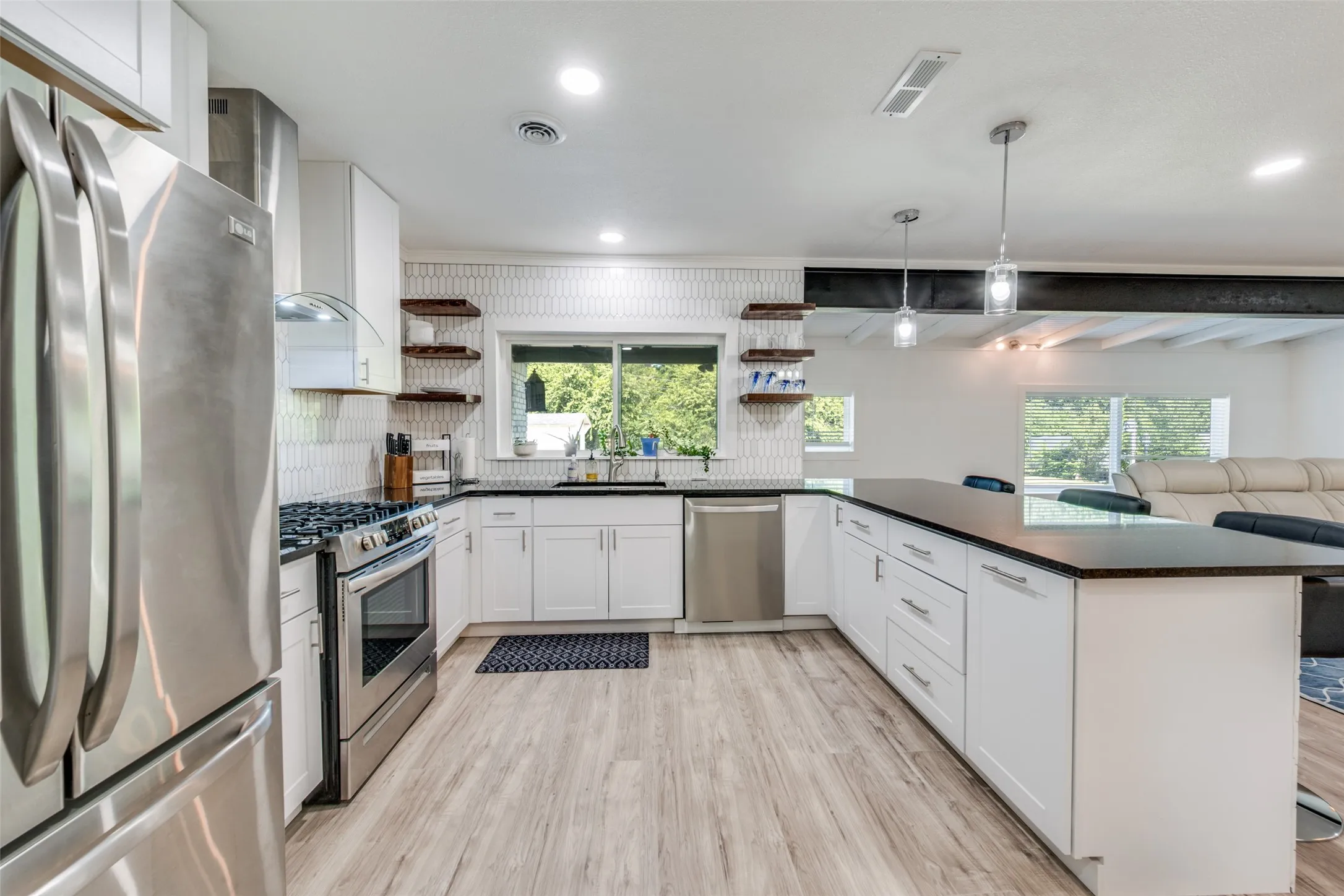 Modern kitchen featuring stainless steel appliances, white cabinetry, dark countertops, wood-finish flooring, and a patterned tile backsplash