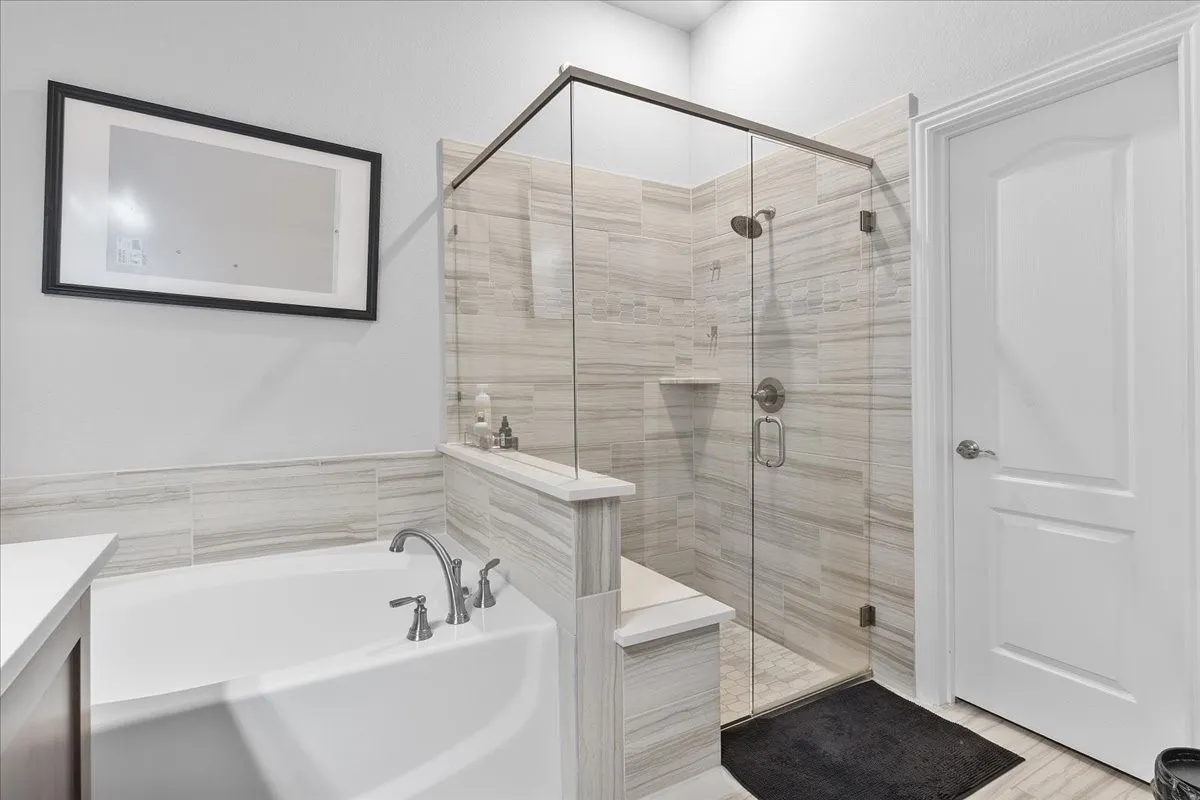 Bathroom featuring a built-in tub with deck-mounted brushed nickel fixtures, a walk-in shower with glass enclosure, light-toned horizontal tile, and a built-in shower​​‌​​​​‌​​‌‌​‌‌​​​‌‌​‌​‌​‌​​​‌​​ bench