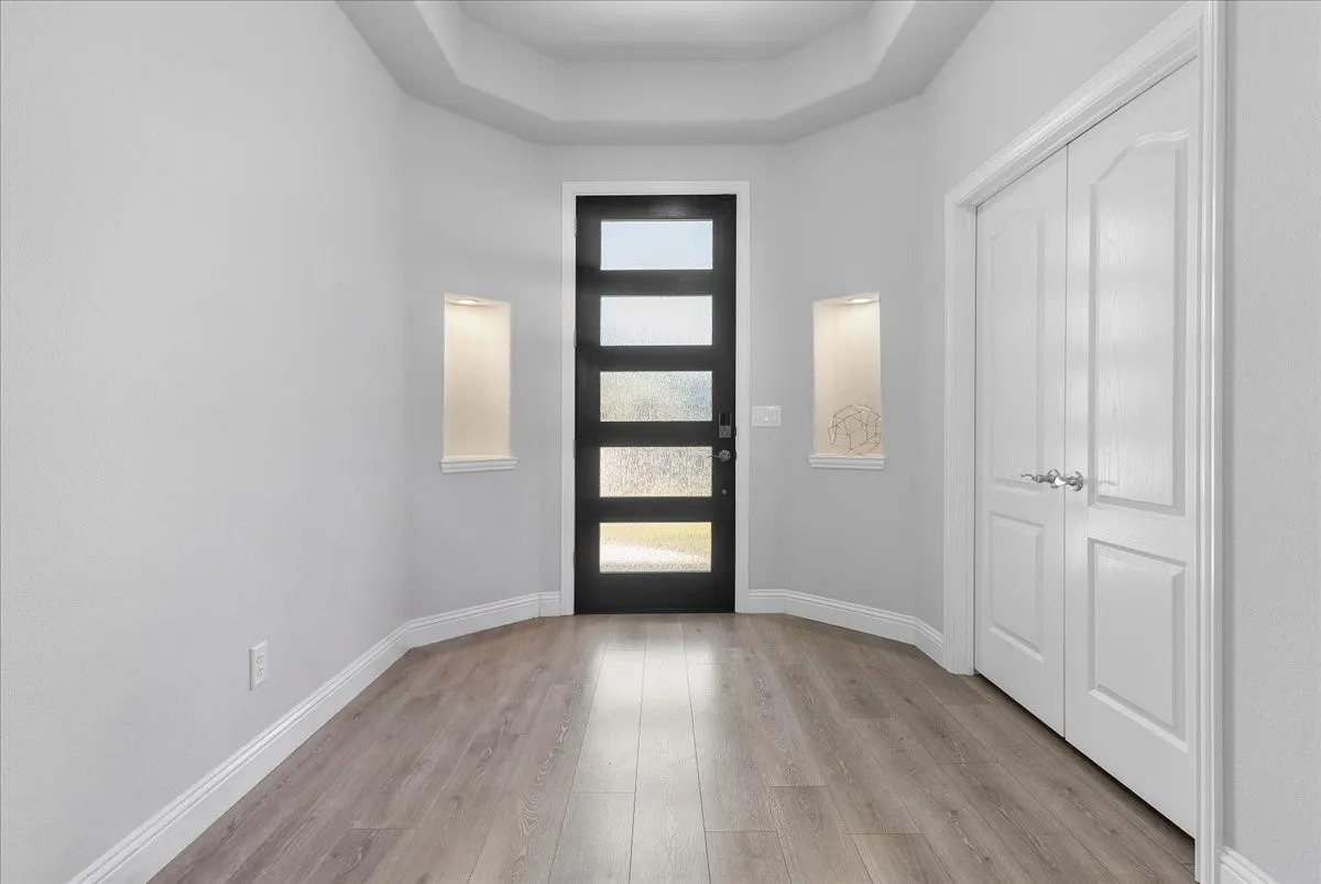 Entryway featuring a contemporary black door with five frosted glass panels, surrounded by two illuminated wall niches