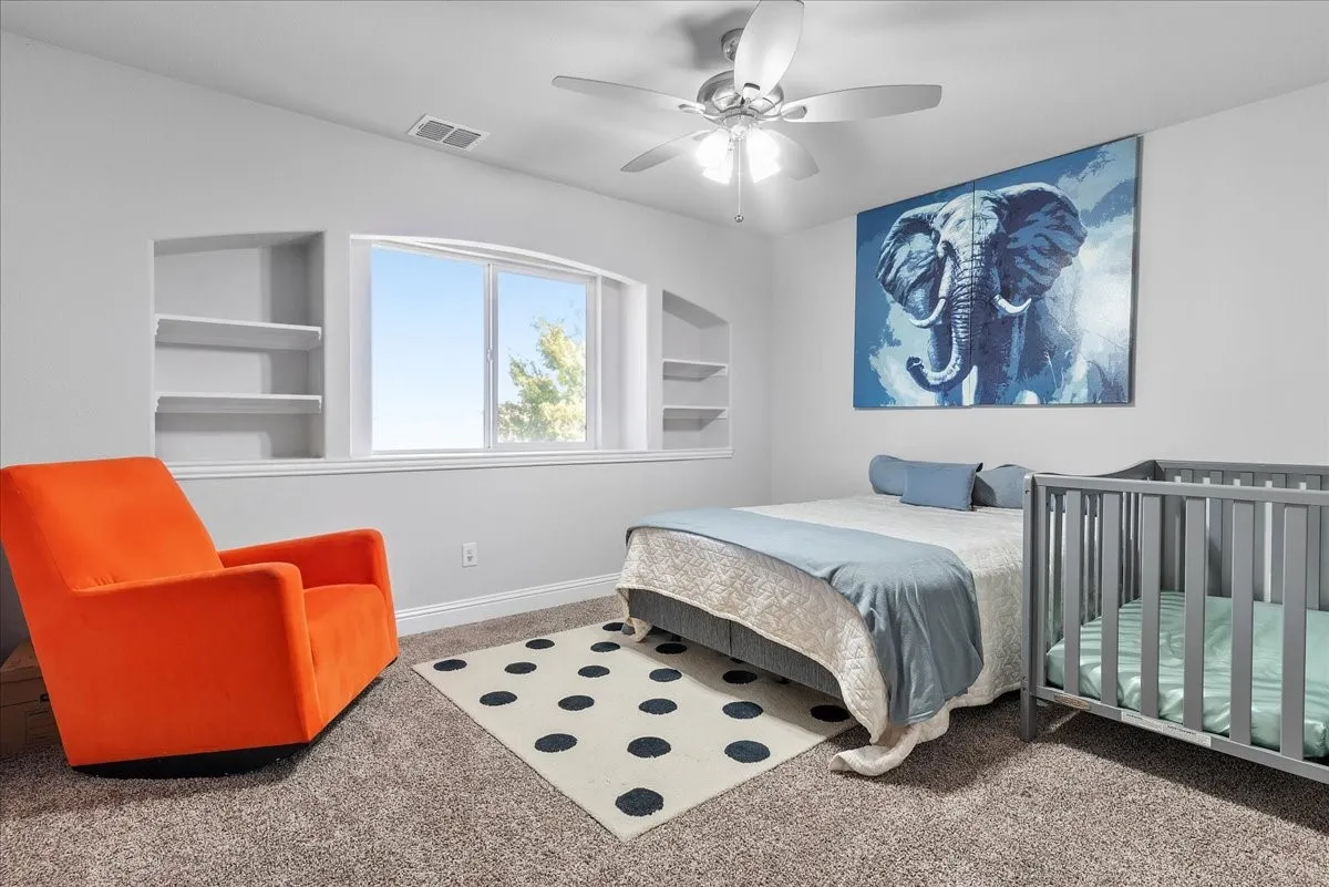 Carpeted bedroom featuring a large window with built-in shelving on either side, a ceiling fan with integrated lighting, and light gray walls
