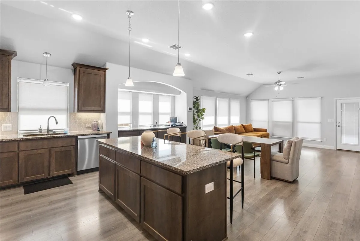 Open-concept living area featuring a kitchen with dark wood-finish cabinetry, a large kitchen island with a stone countertop, stainless steel appliances, and wood-finish flooring throughout