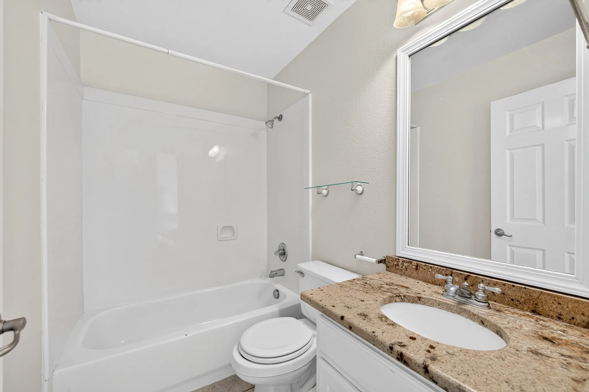 Bathroom featuring a bathtub and shower surround, a toilet, a vanity with a granite countertop and integrated sink, and a framed mirror