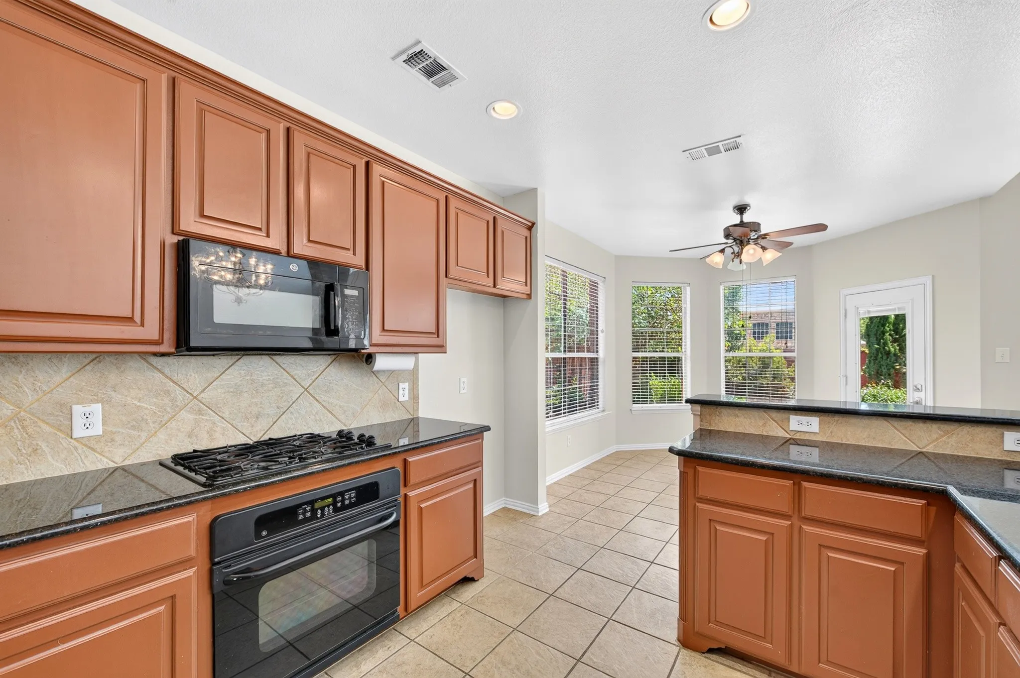 Kitchen featuring warm-toned cabinetry, dark countertops, and a tiled backsplash