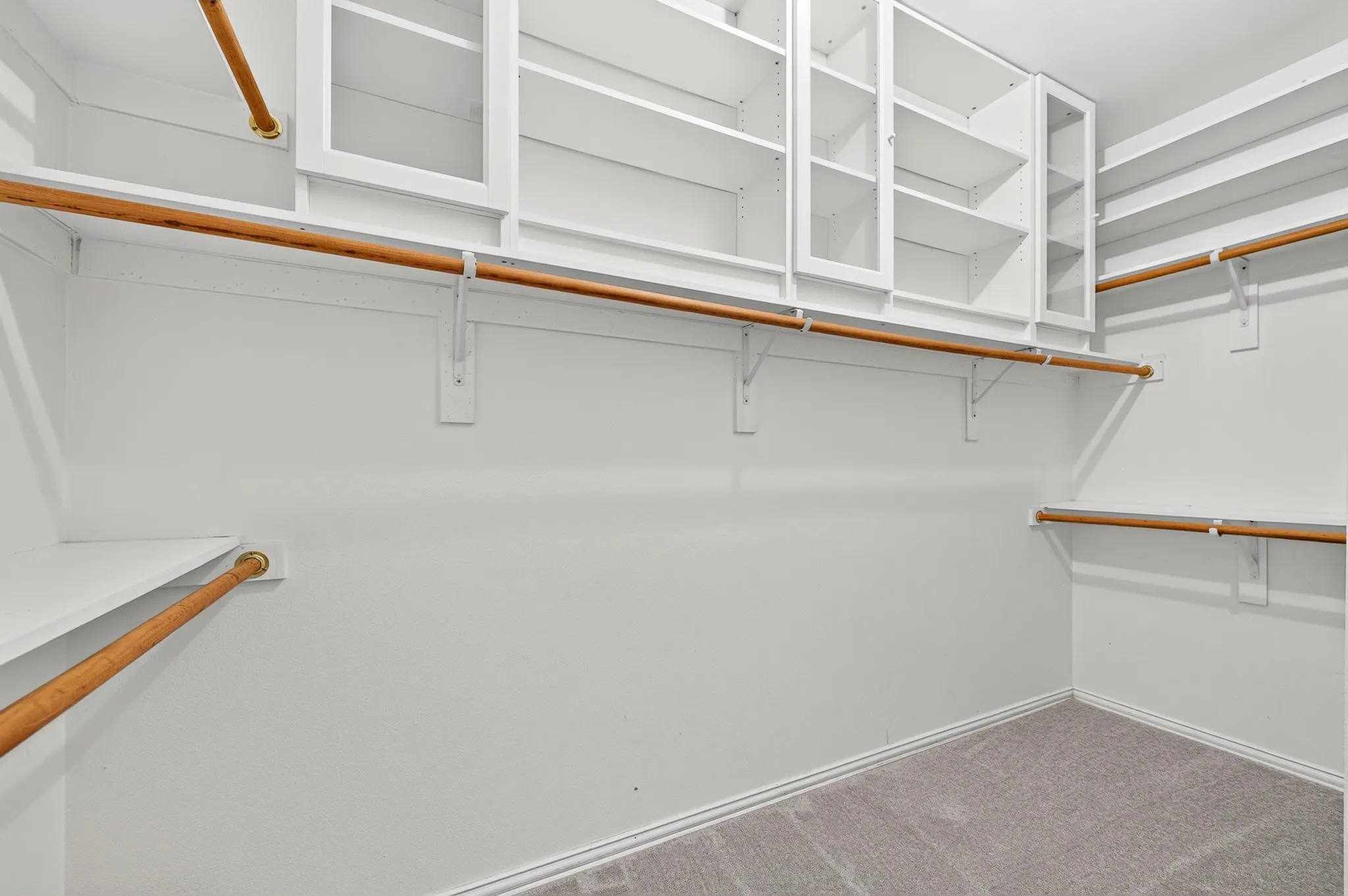 Primary walk-in closet featuring built-in white shelving, multiple hanging rods, and an integrated cabinet system with glass-front doors