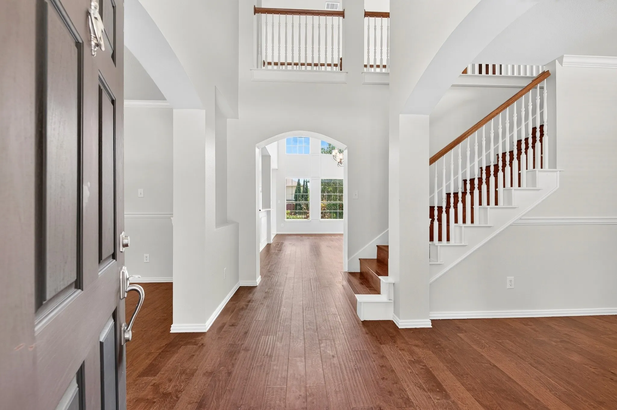 Two-story foyer featuring wood-finish flooring, a grand staircase with white balusters and a wood handrail, arched entryways, and abundant natural light from upper and lower windows