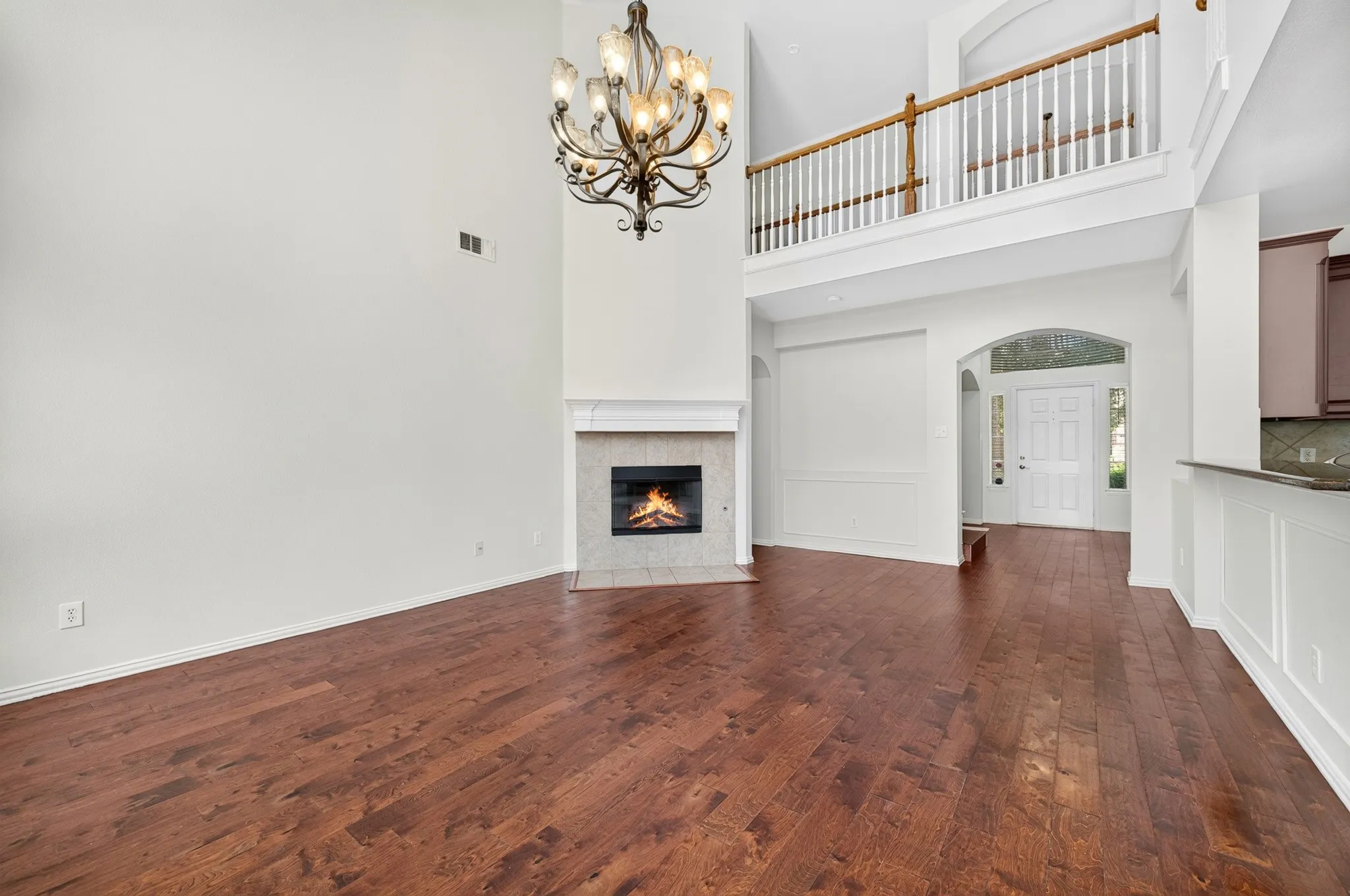 Vaulted ceiling space featuring wood-finish flooring, a decorative chandelier, and a fireplace with a stone surround