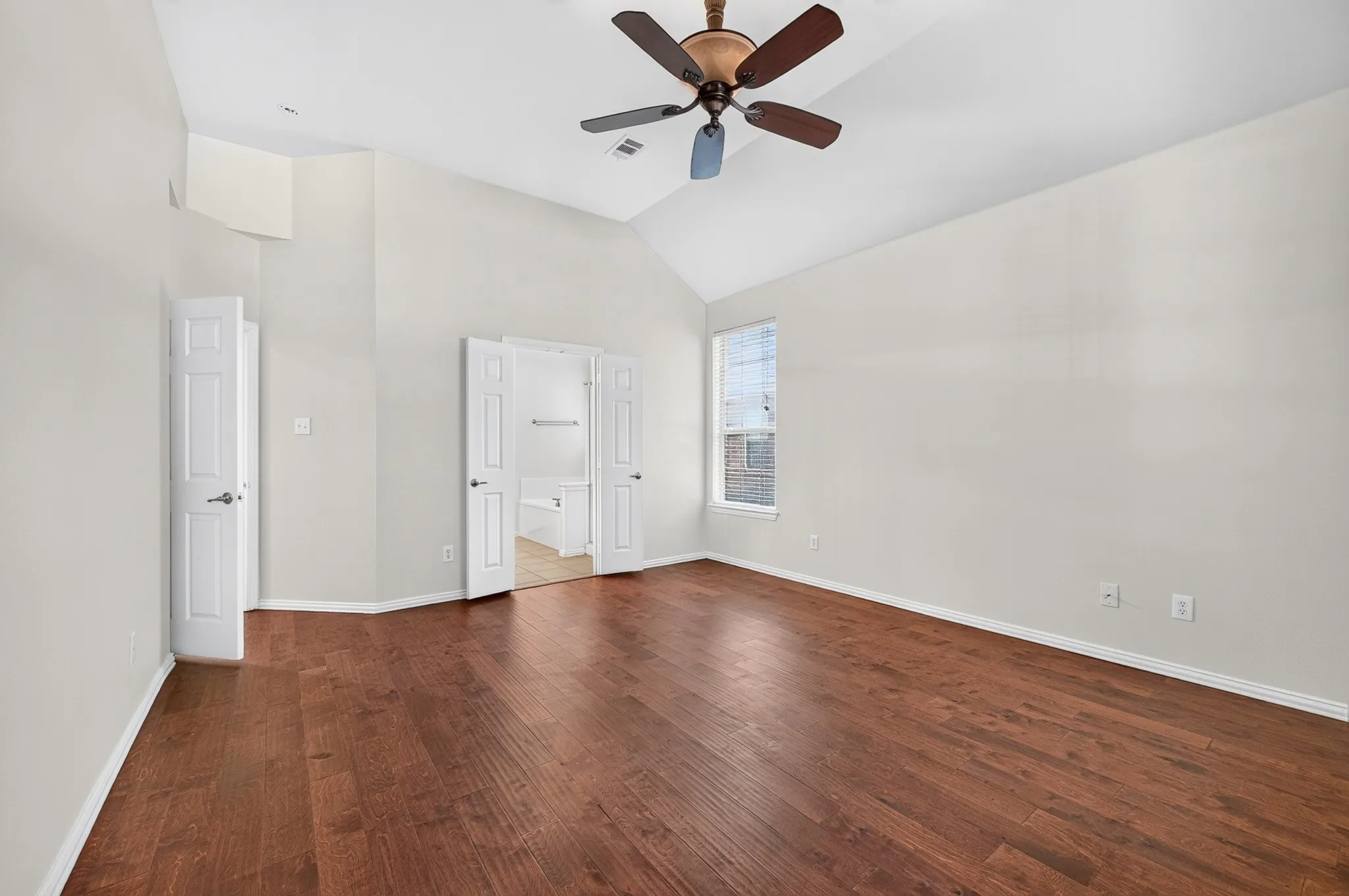 Spacious room featuring wood-finish flooring, a vaulted ceiling, and a ceiling fan with integrated lighting