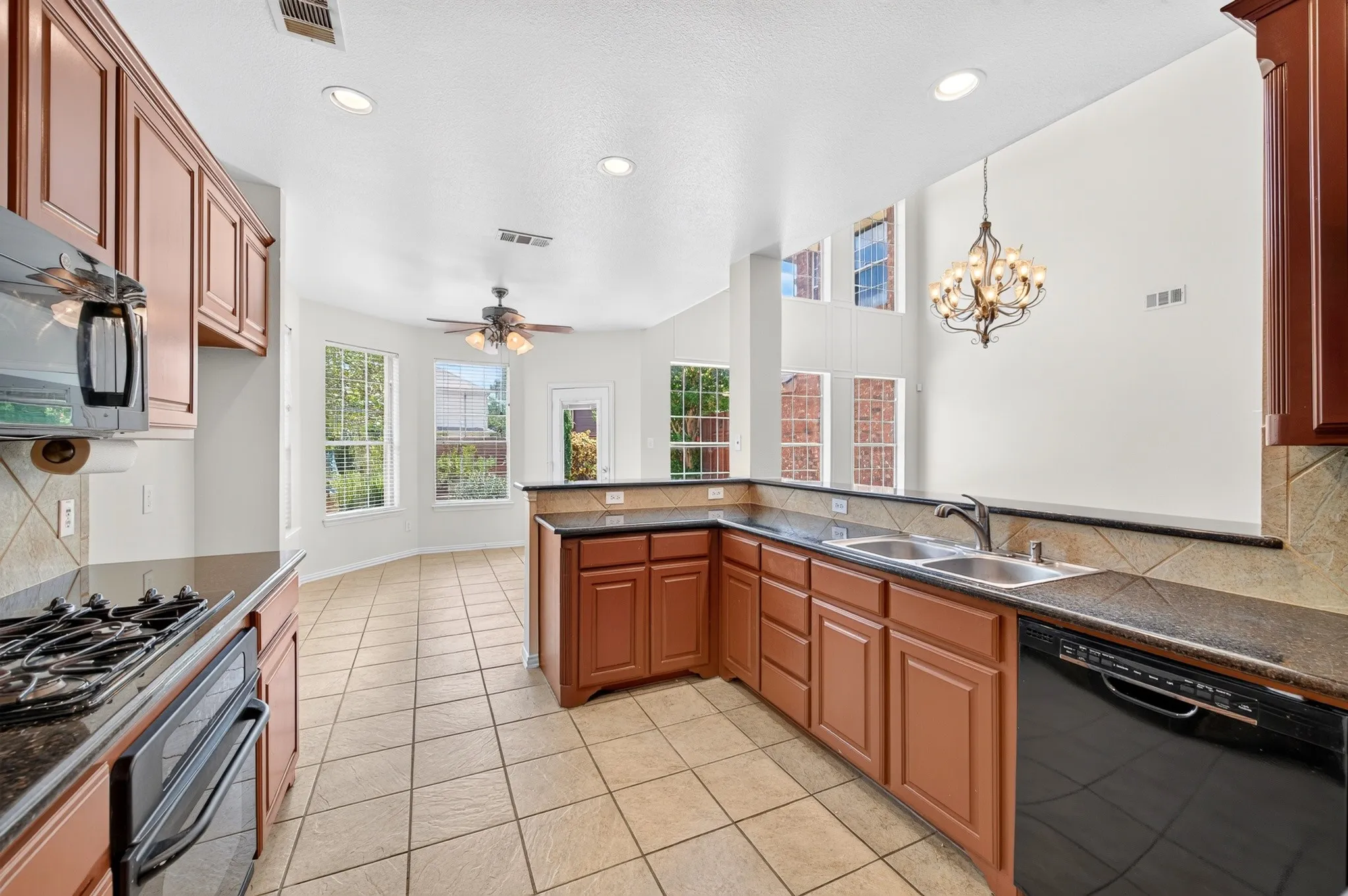 Kitchen featuring a gas range, dark countertops, wood cabinetry, tile flooring, and a stainless steel double basin sink