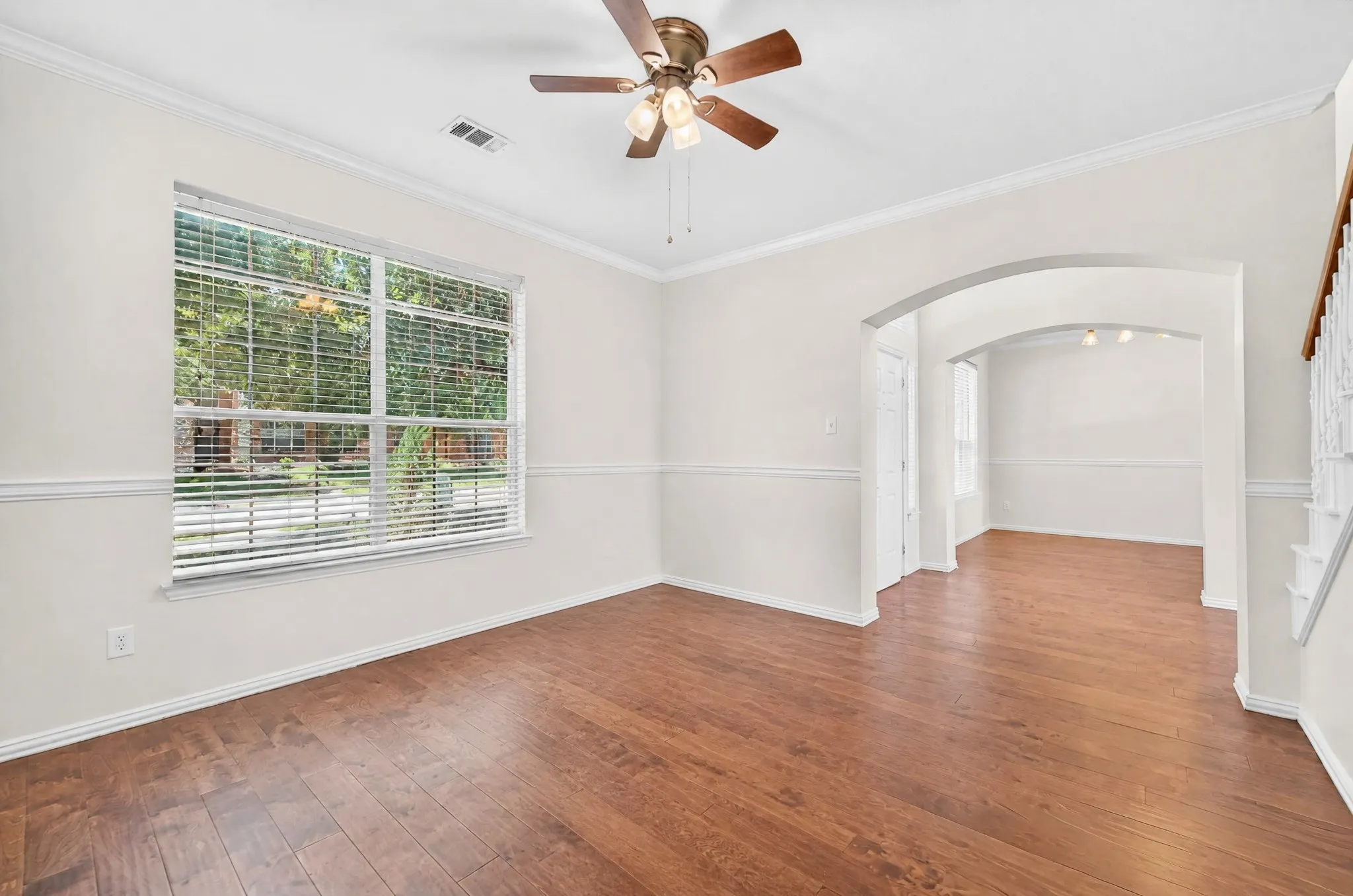 Spacious room featuring wood-finish flooring, a large window with blinds, crown molding, a ceiling fan, and an arched entryway
