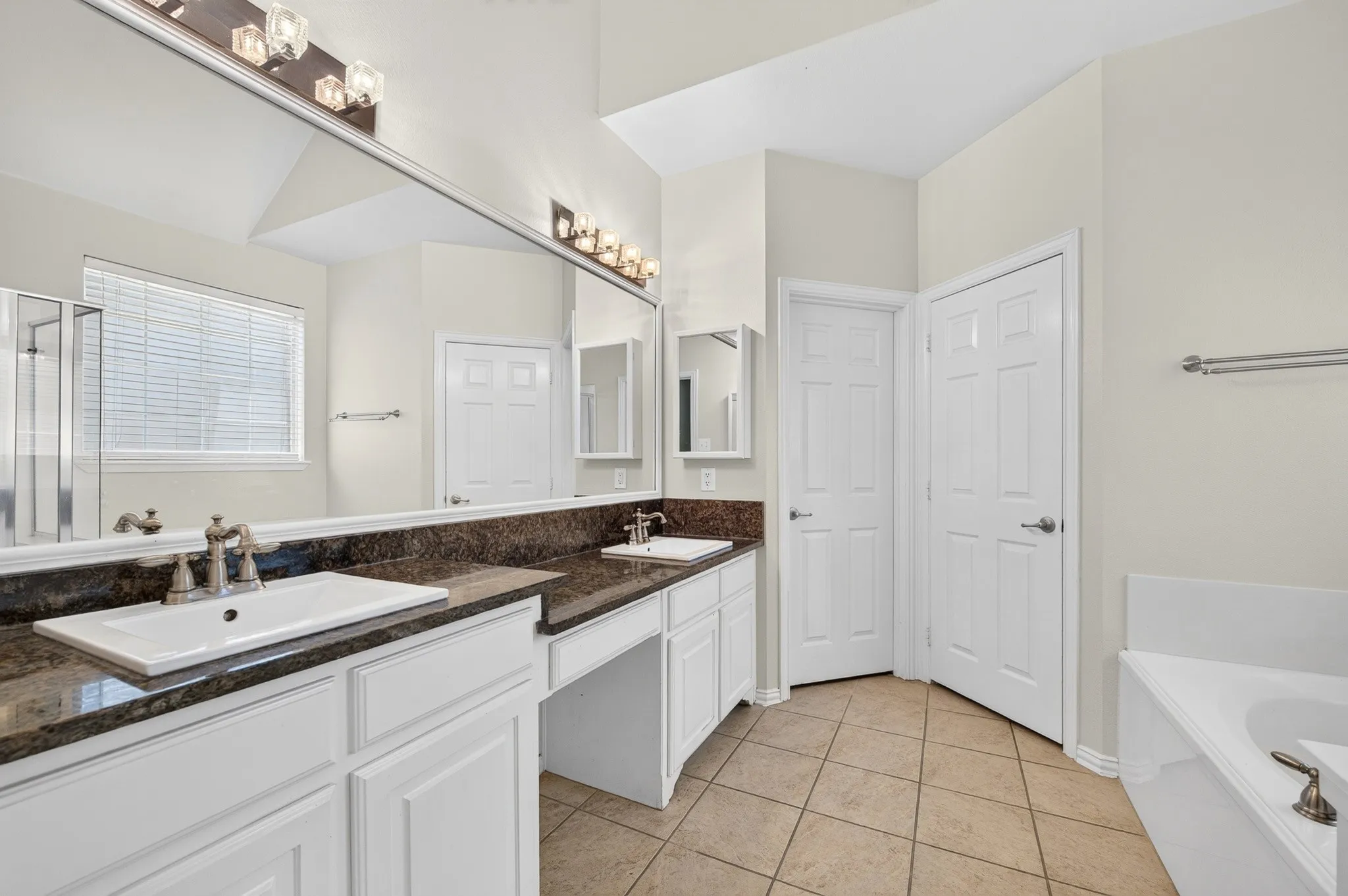 Bathroom featuring a dual vanity with undermount sinks, stone countertops, and white cabinetry