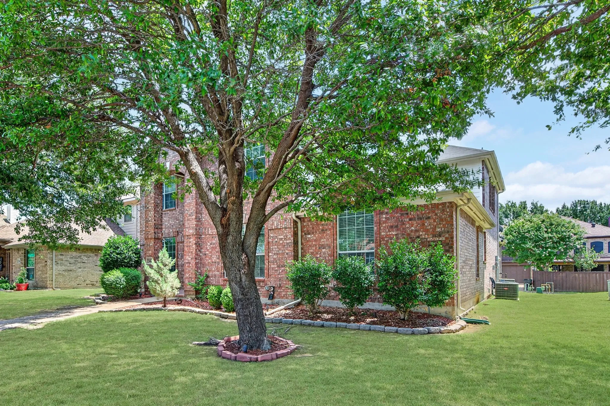 Mature tree anchoring a manicured lawn, complemented by a brick facade and decorative landscaping