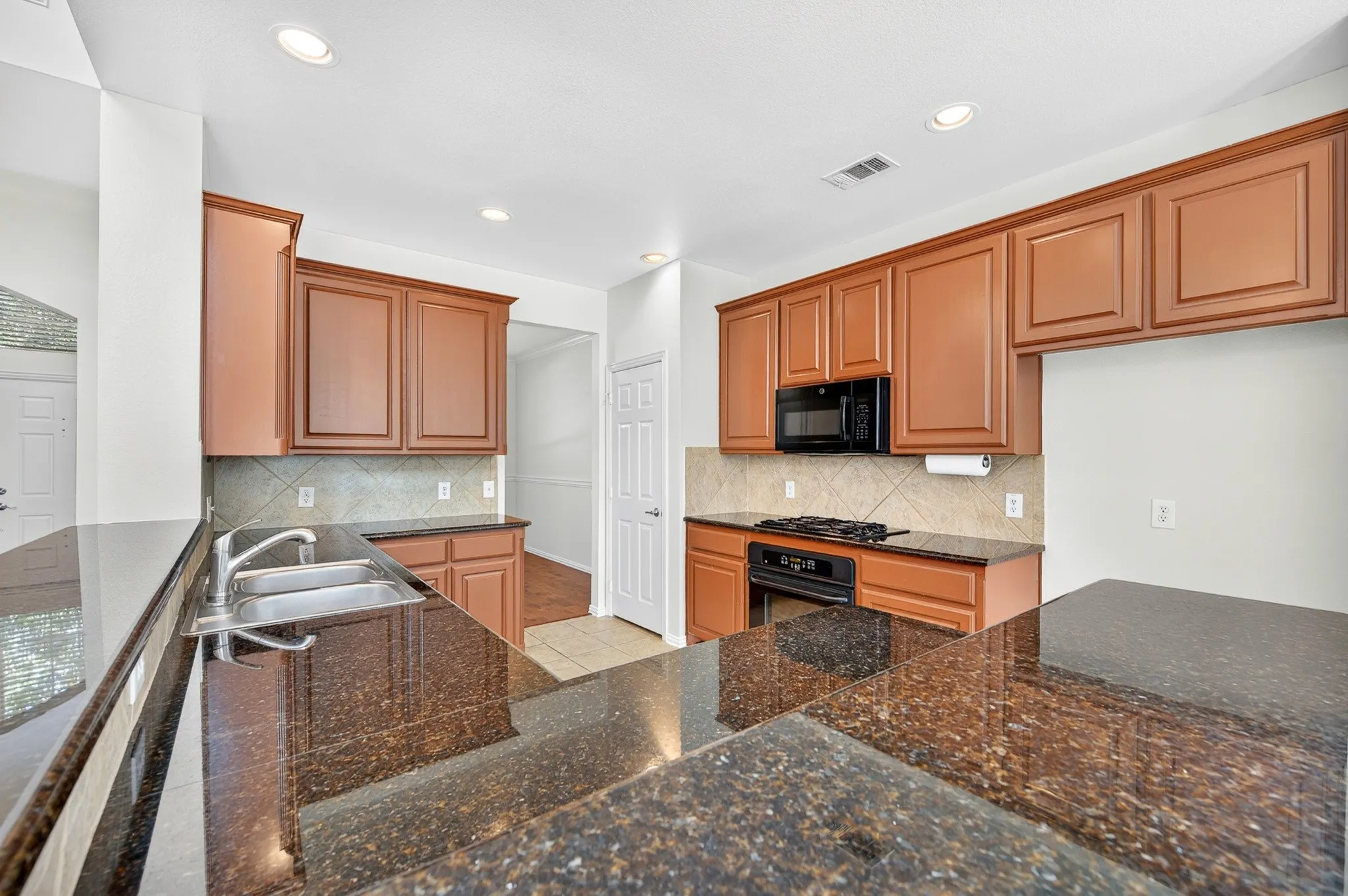 Kitchen featuring extensive dark granite countertops, rich wood cabinetry, stainless steel double basin sink, black built-in microwave, and a gas range