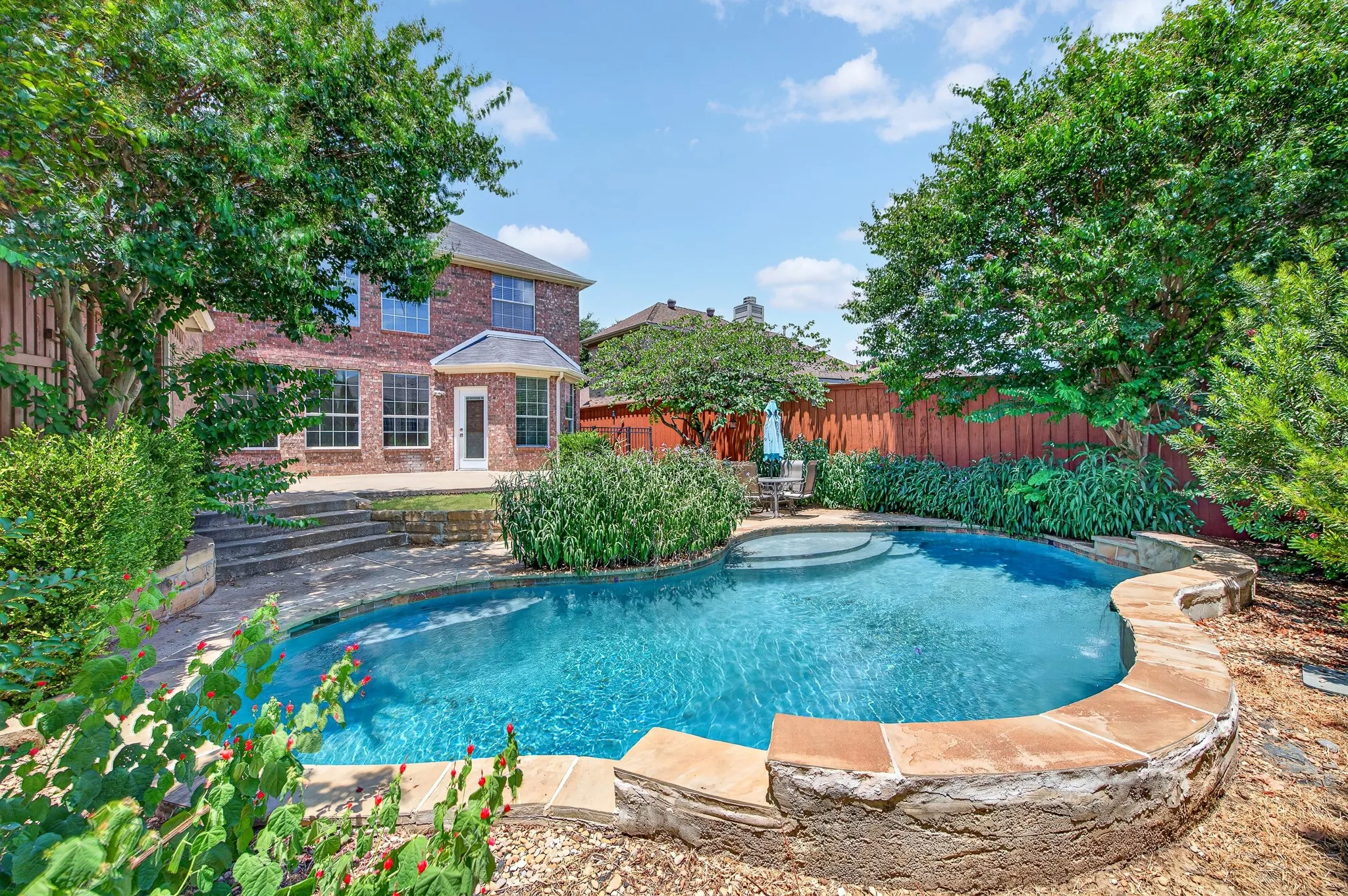 Curved swimming pool with an integrated spa, surrounded by natural stone coping and a stone-clad retaining wall