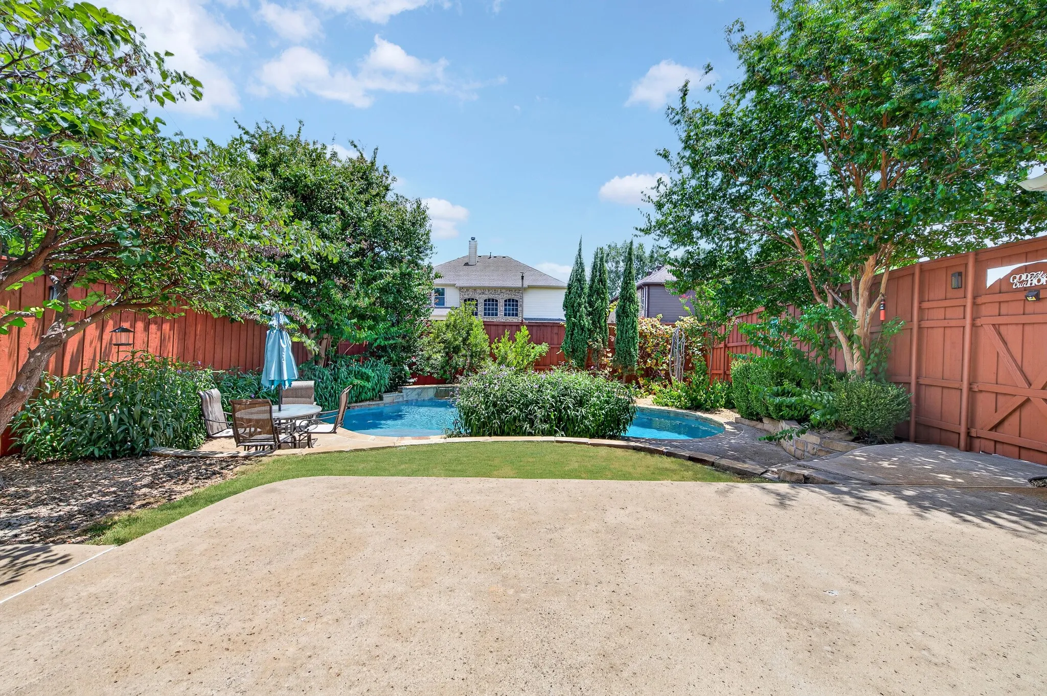 Backyard featuring a swimming pool with stone coping, a surrounding privacy fence, mature trees, and established landscaping