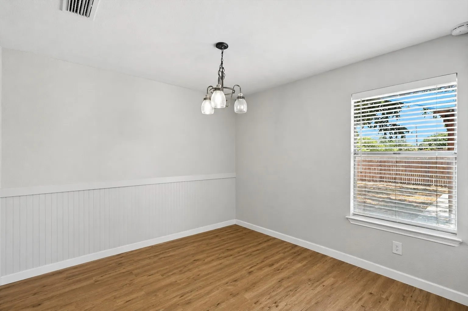 Room featuring wood-finish flooring, white baseboards, and beadboard wainscoting