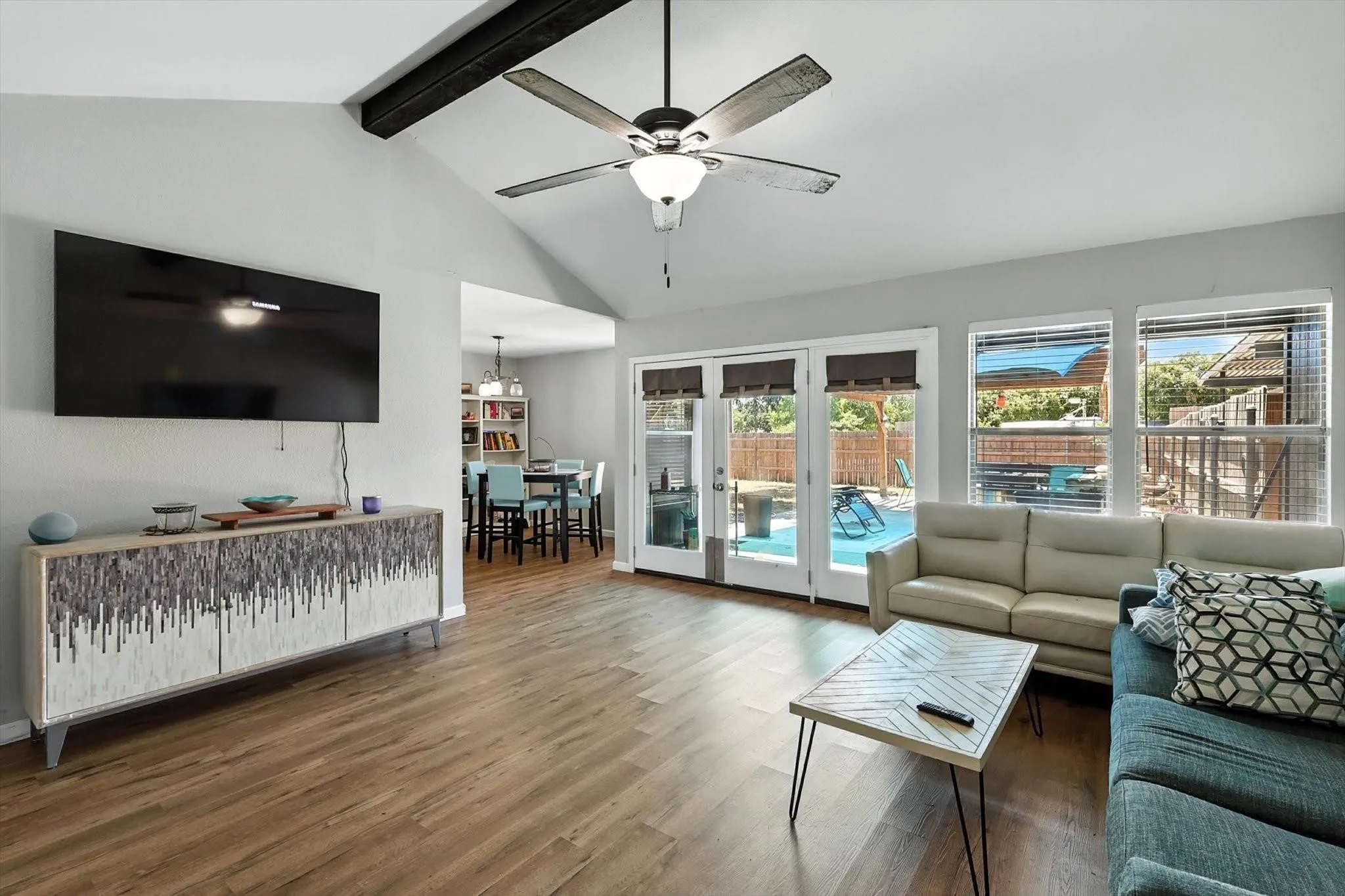 Vaulted ceilings featuring an exposed beam, wood-finish flooring, and French doors leading to a private pool