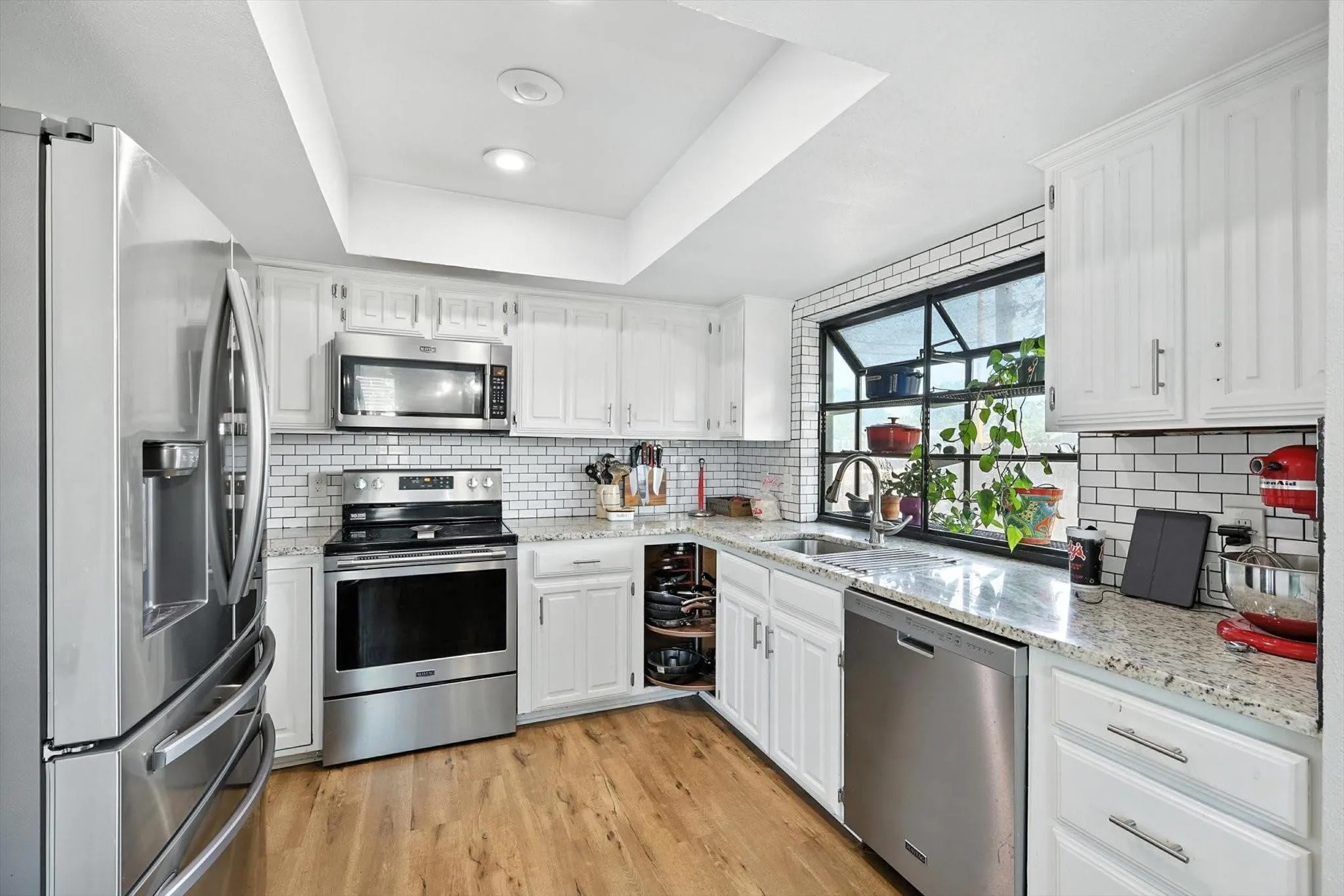 Recessed ceiling lighting, white cabinetry with T-bar pulls, white subway tile backsplash, granite countertops, and wood-finish flooring