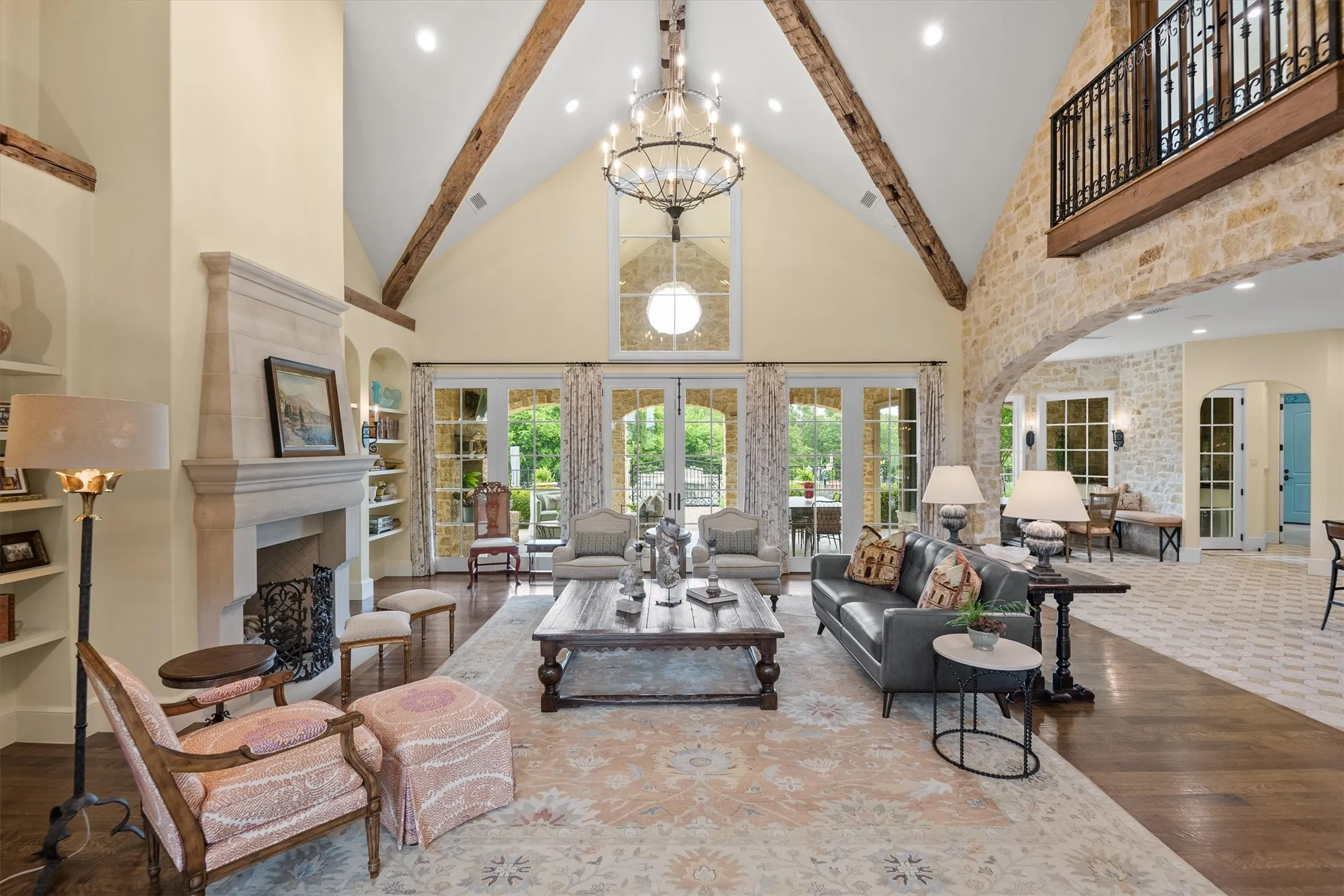 The dramatic, soaring, vaulted ceiling of the great room is further enhanced by reclaimed wooden beams, a large concrete fireplace, a Juliet balcony above and wide open windows looking out to the expansive outdoor living area and pool.