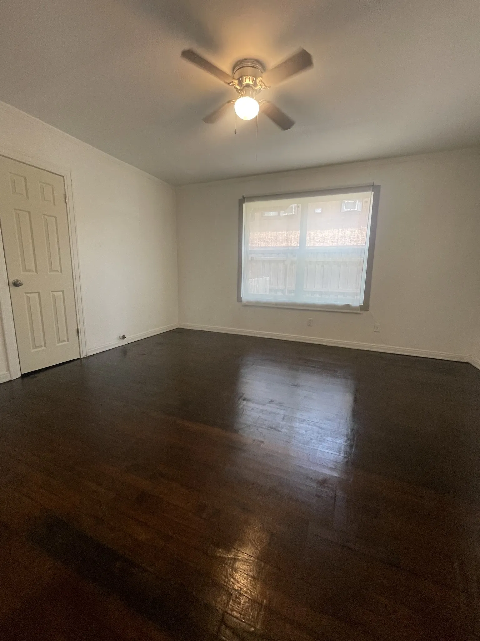 Dark wood-finish flooring, white walls, and a ceiling fan with integrated lighting