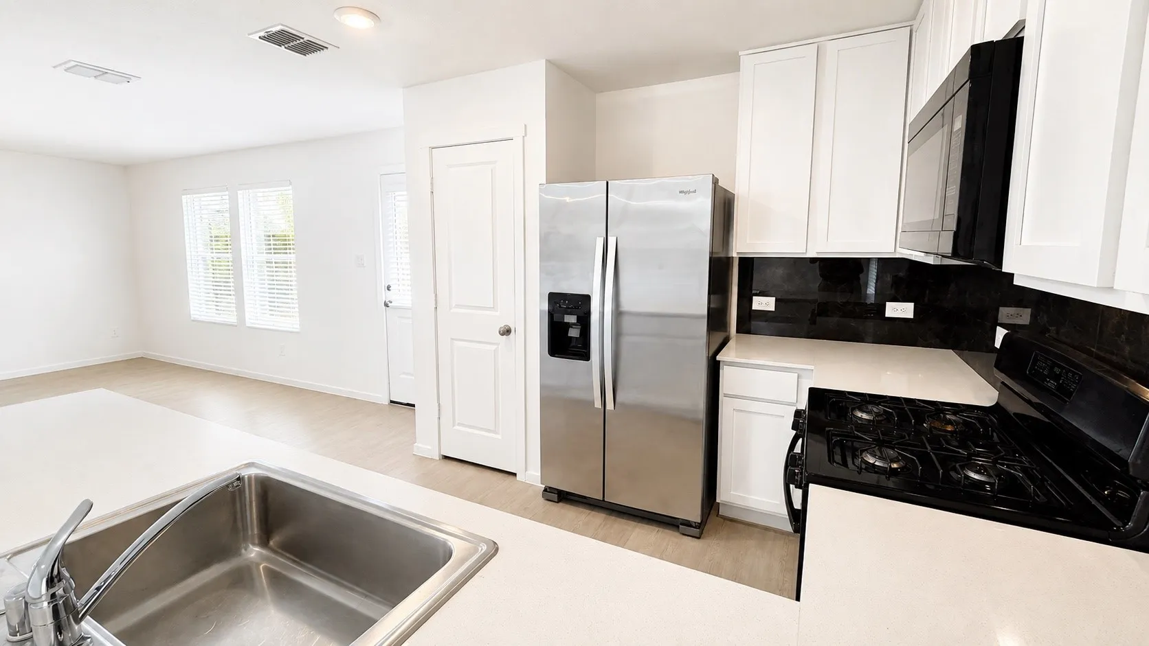Kitchen featuring a stainless steel refrigerator, dark backsplash, gas range, white cabinetry, and light countertops