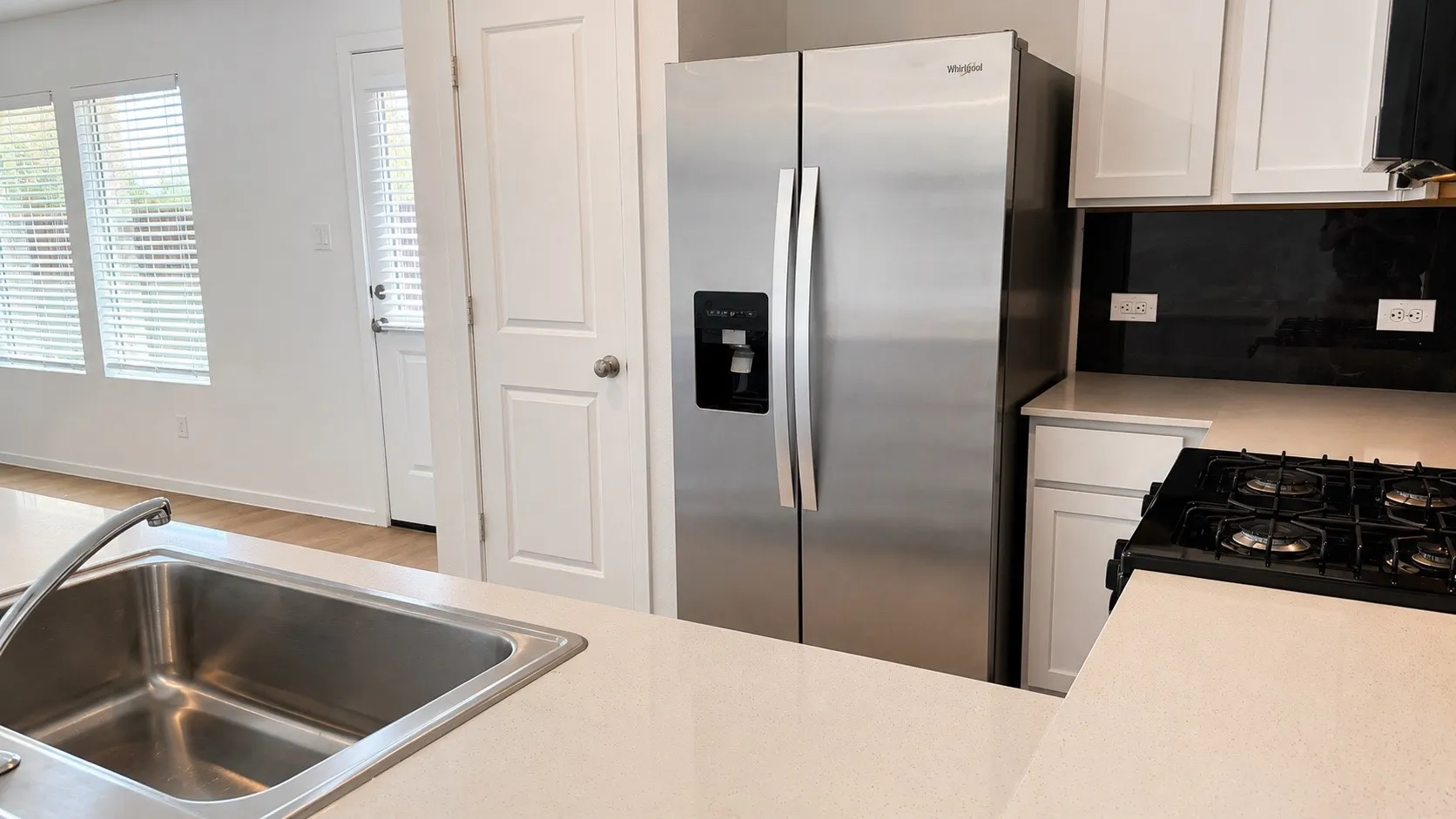 Stainless steel side-by-side refrigerator, gas cooktop, white shaker cabinetry, light-toned countertops, and a stainless steel sink
